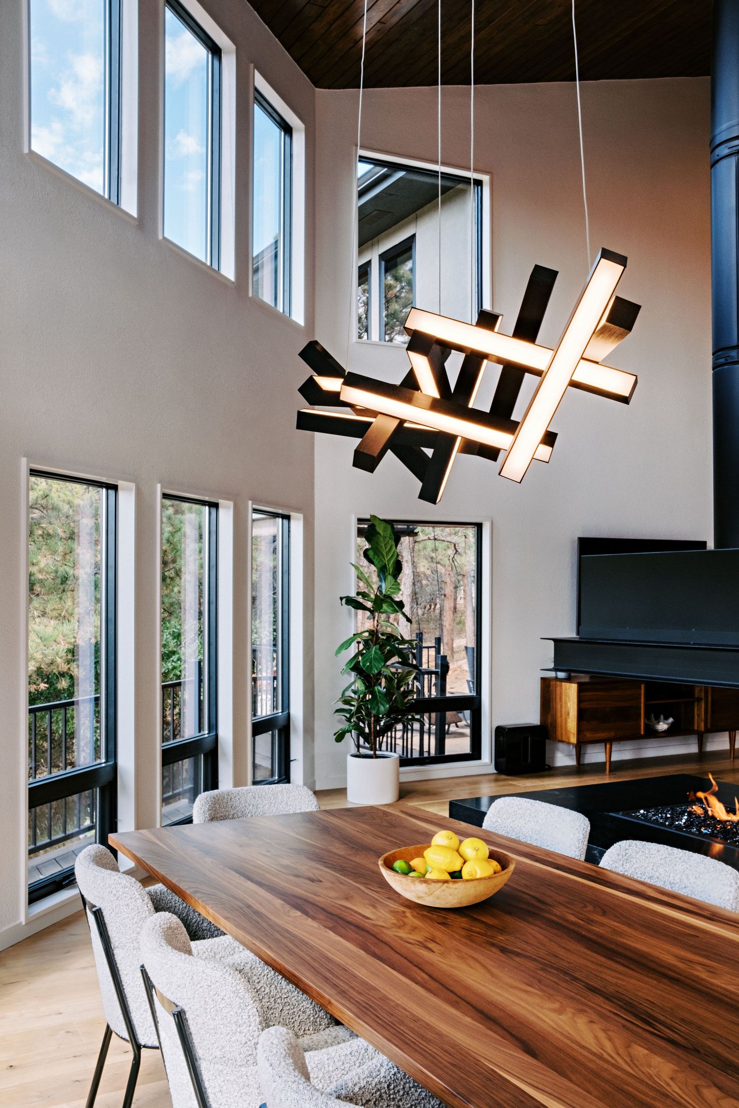 Contemporary dining area featuring unique black geometric pendant lights and walnut table beneath tall windows.