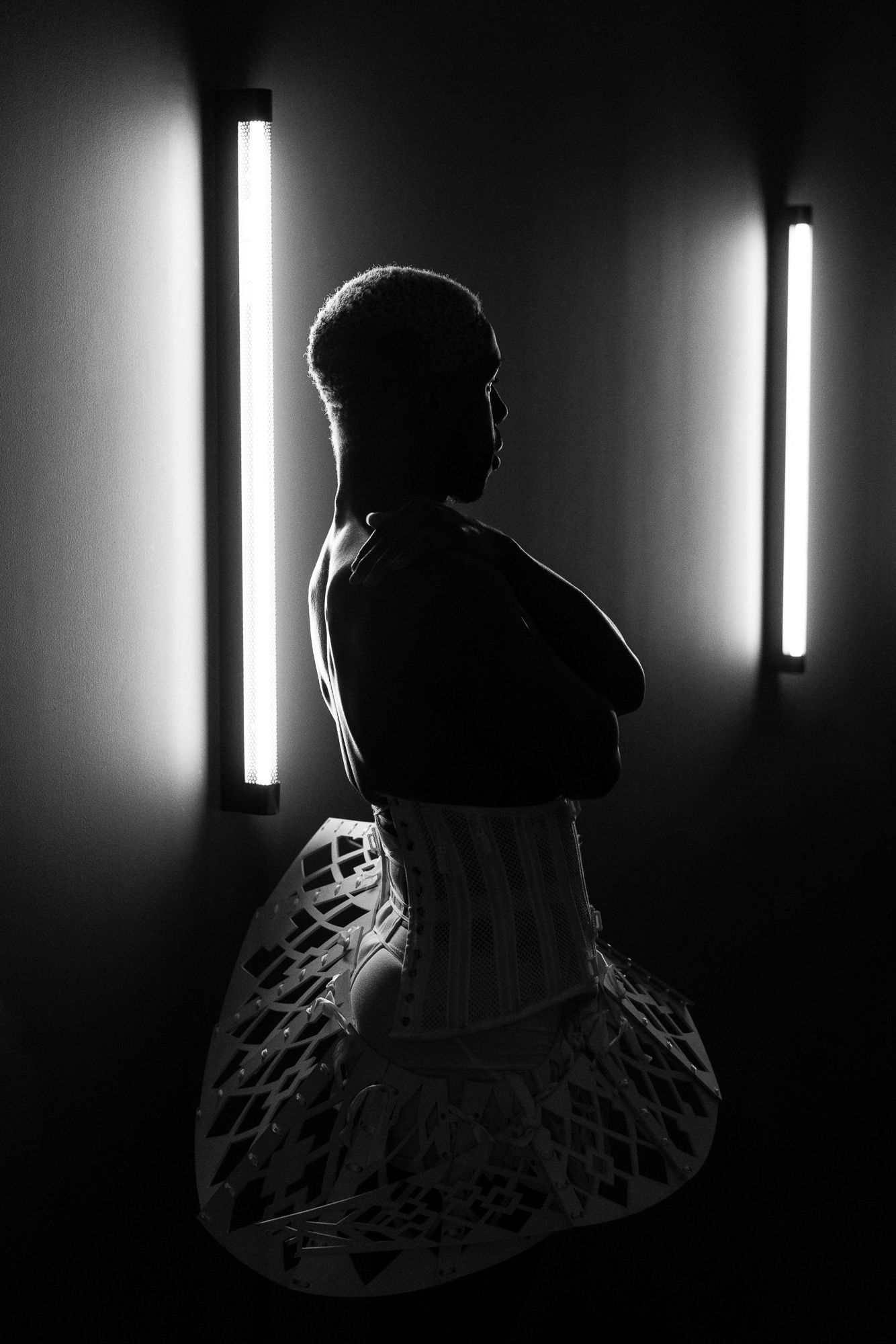 Dramatic silhouette of figure against glowing vertical light tubes in dark setting.