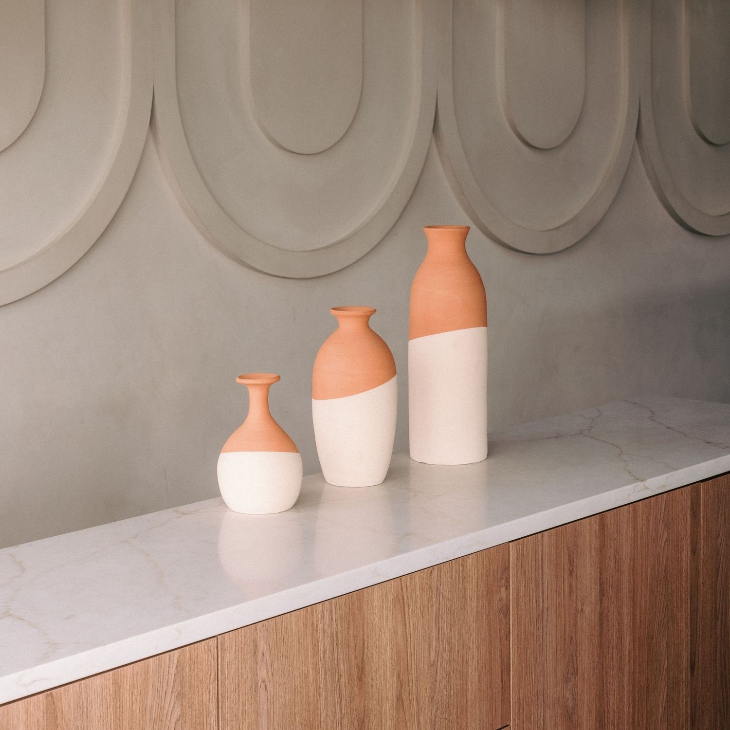 Decorative ceramic vases in terracotta and white displayed on wooden shelf with wall detail.