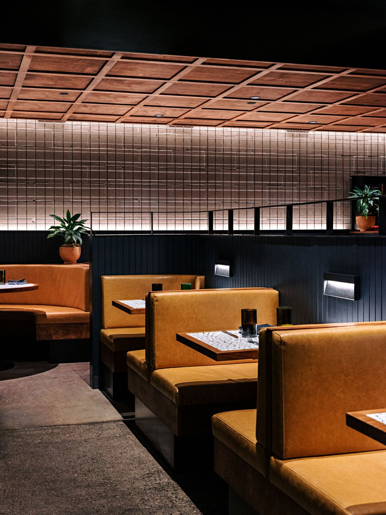 Cozy restaurant booth seating with tan upholstery against tiled wall and wooden ceiling detail.