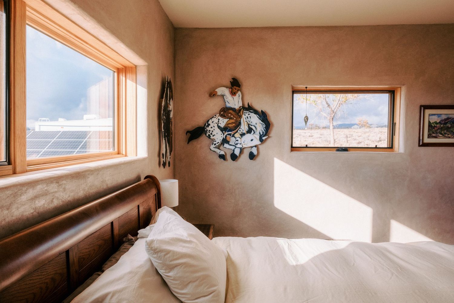 Cozy bedroom interior with sunlit window and decorative wall art in warm earth tones.