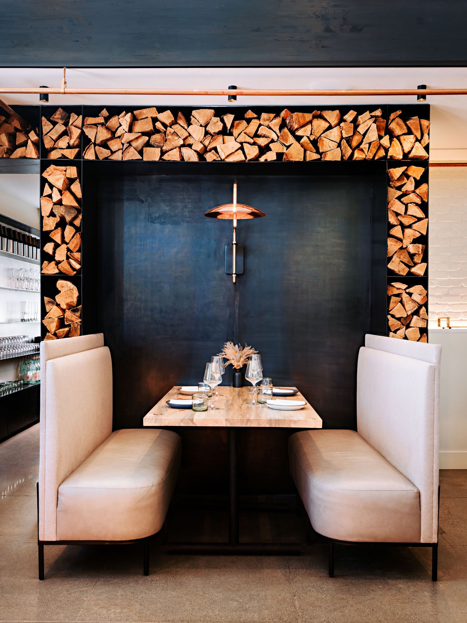 Sleek restaurant dining area with white booth seating and decorative firewood wall accents.
