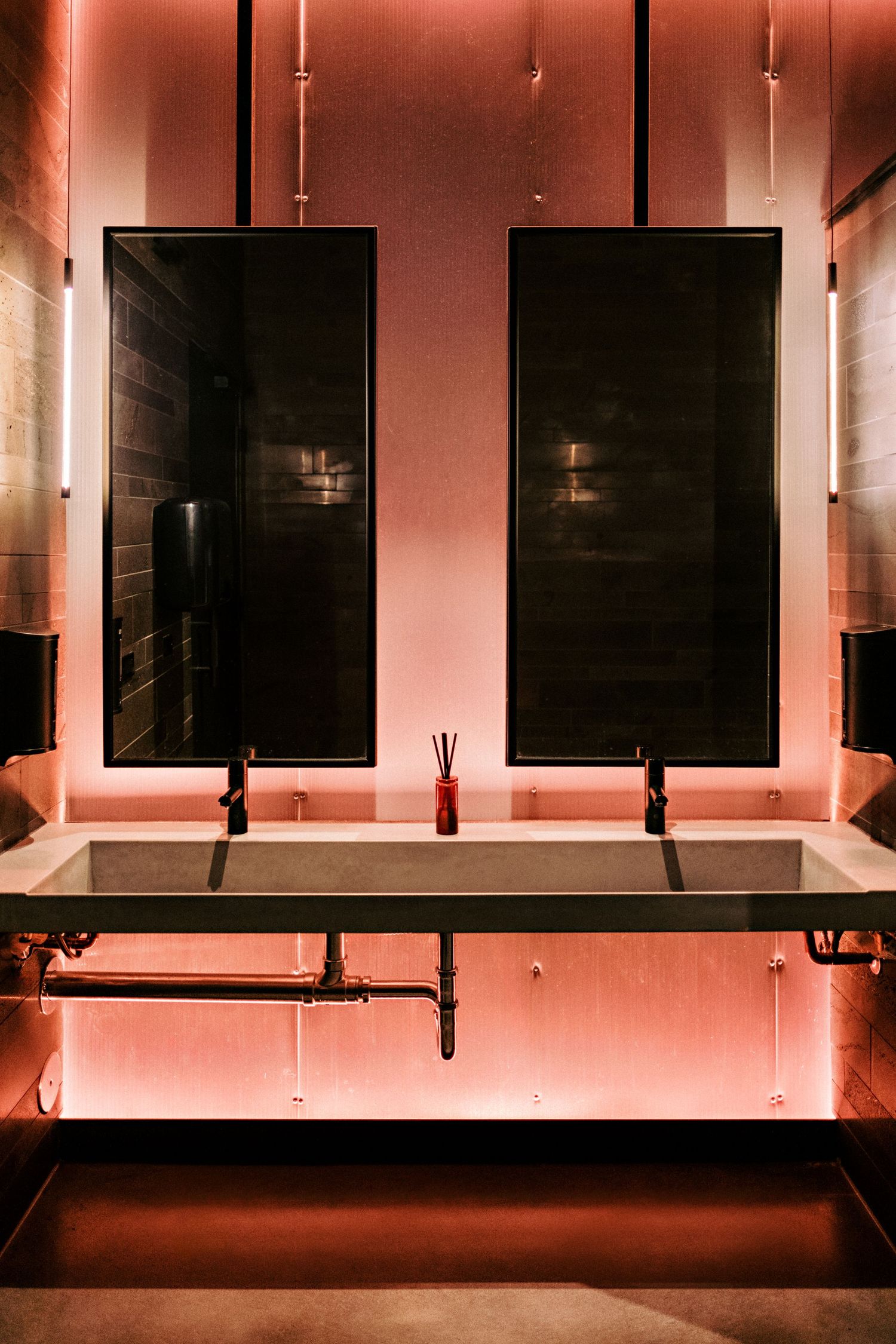Row of mounted black TV screens against a wall illuminated with pink accent lighting.