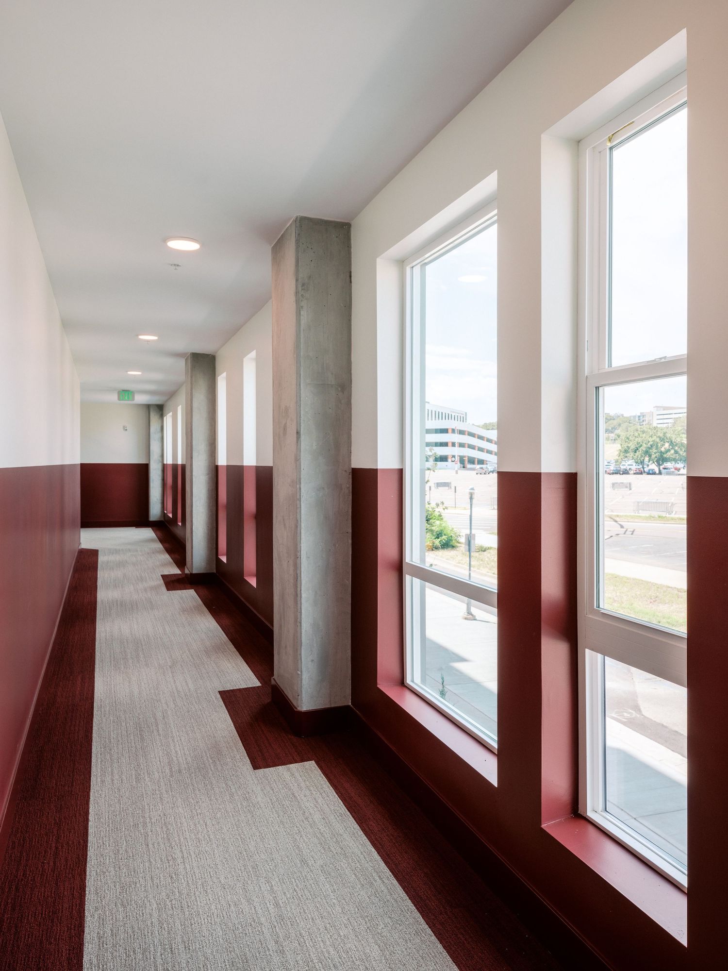 Long corridor with red accent walls and large windows creating a bright, modern atmosphere.