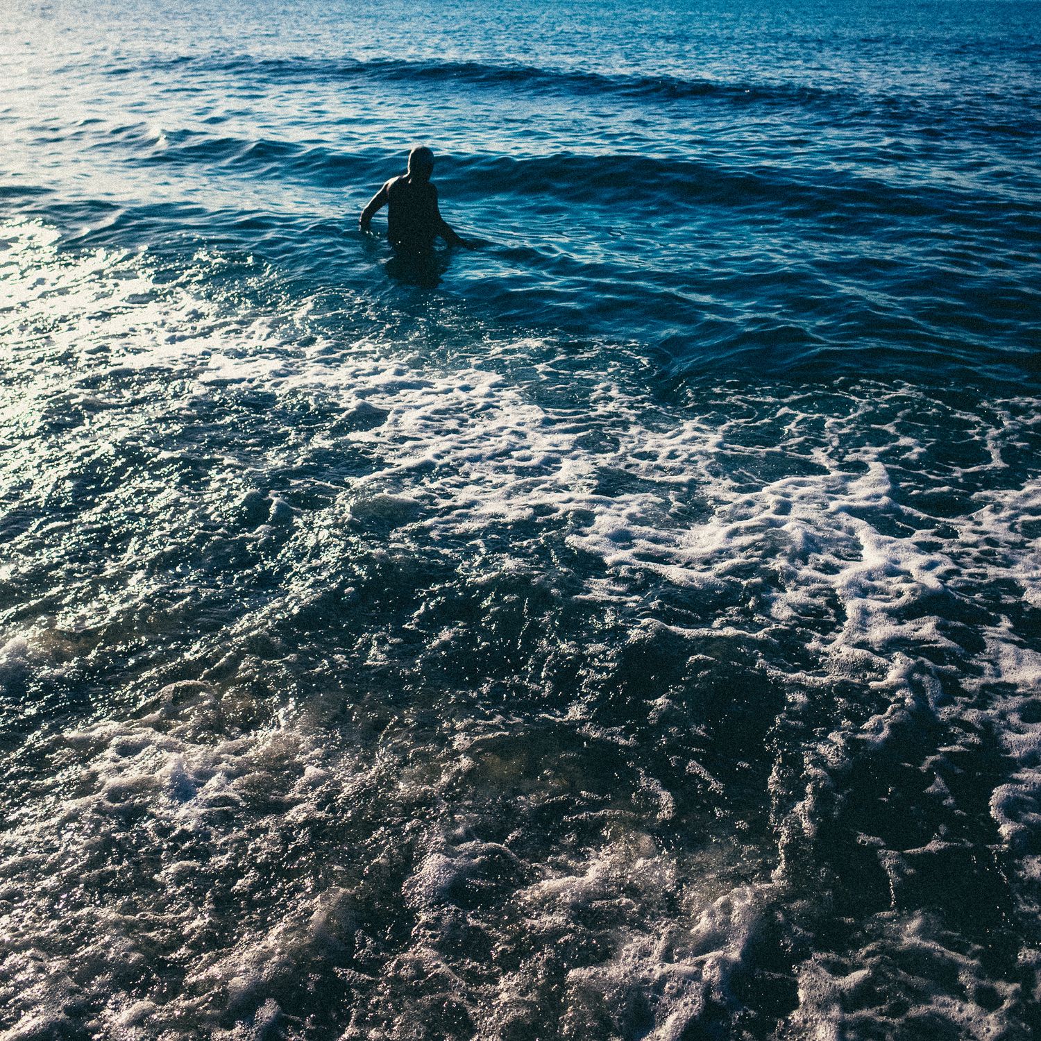Aerial view of dark blue ocean waves with sunlight reflecting off the rippling water surface creating a dynamic pattern.