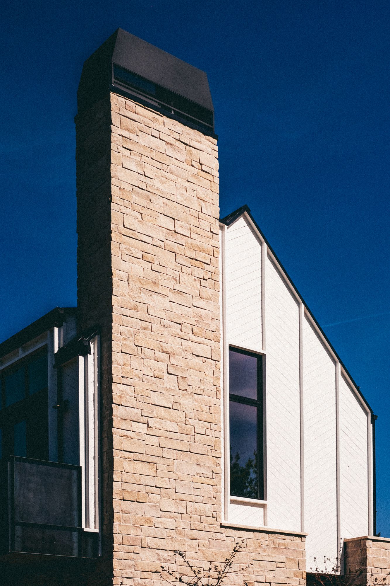 Modern home exterior featuring a tall stone chimney with beige stacked stone against a deep blue sky.