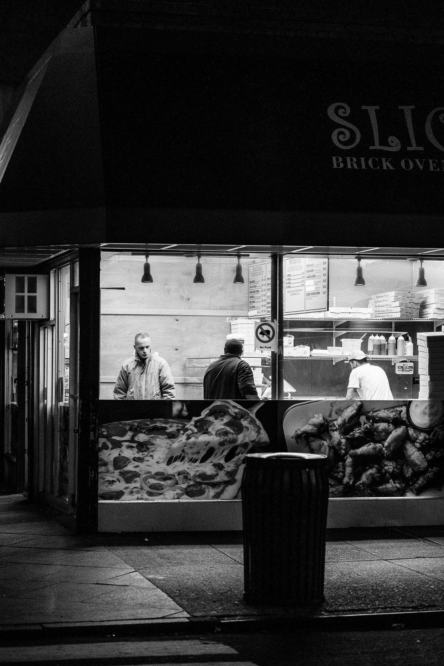 A black and white photo series showing a dimly lit storefront window display at night with silhouettes of passersby.