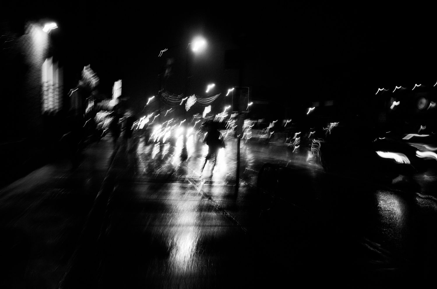 Blurred black and white street scene at night with silhouettes and glowing lights.