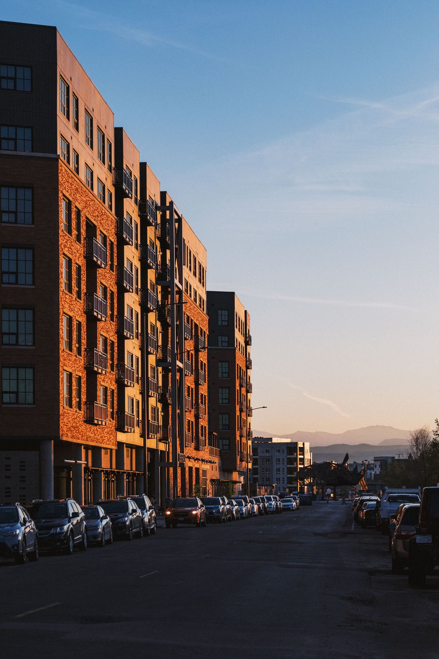 Red brick residential complex with dark accents photographed at golden hour with parked cars.