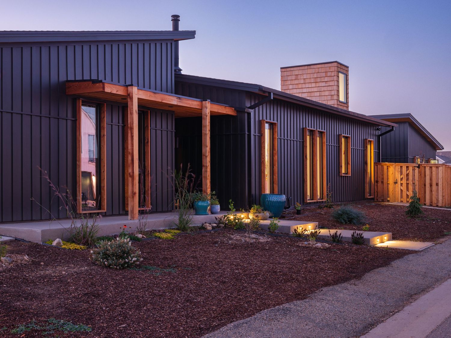 Dusk view of contemporary architecture featuring dark exterior and warm window lighting.