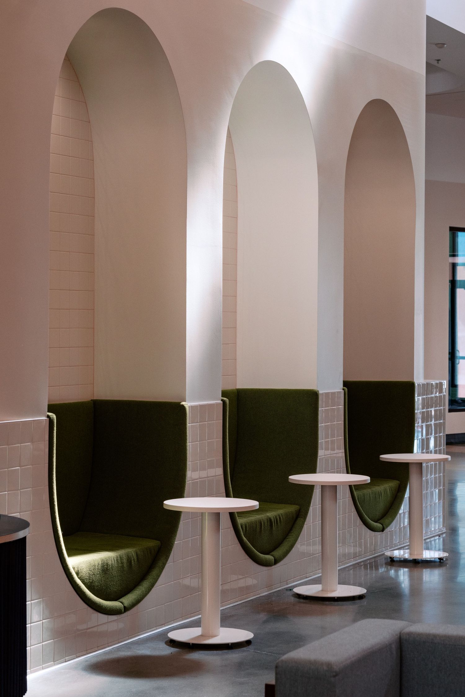Modern seating alcoves with arched designs, green cushions, and white pedestal tables.