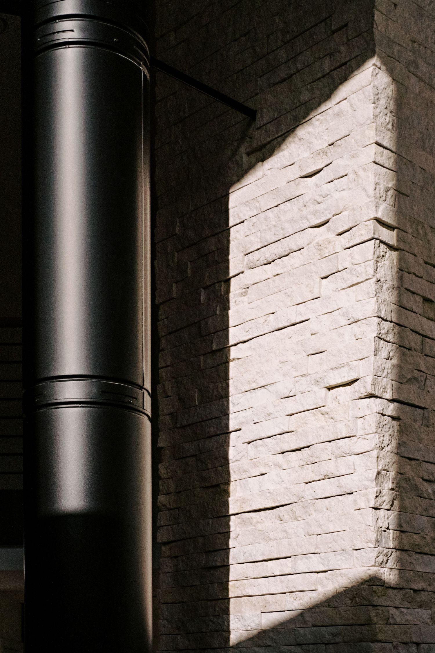 Close-up detail of black metal chimney pipe against textured white stone wall.