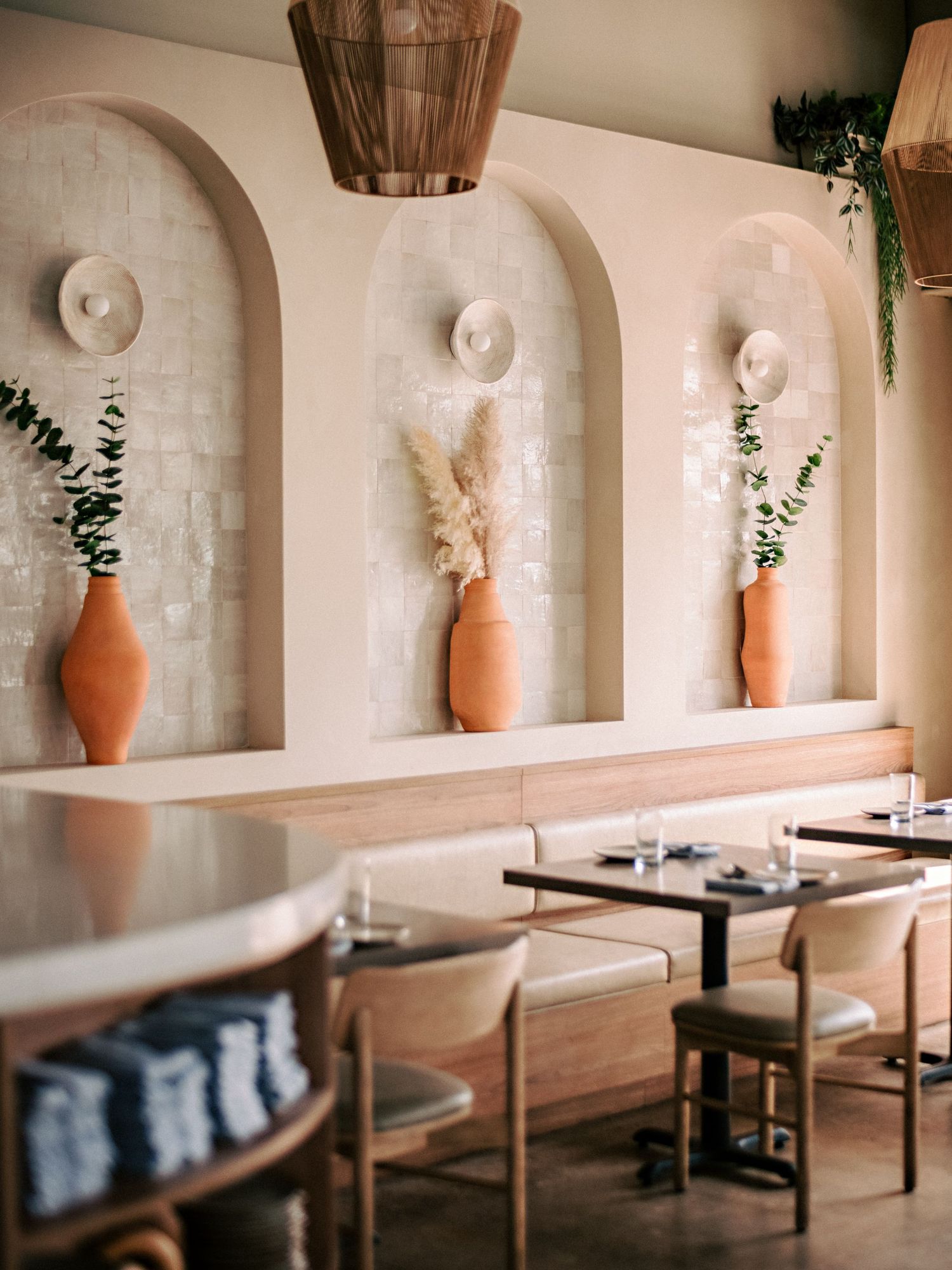 Minimalist dining area featuring arched wall niches with terracotta vases and greenery accents.