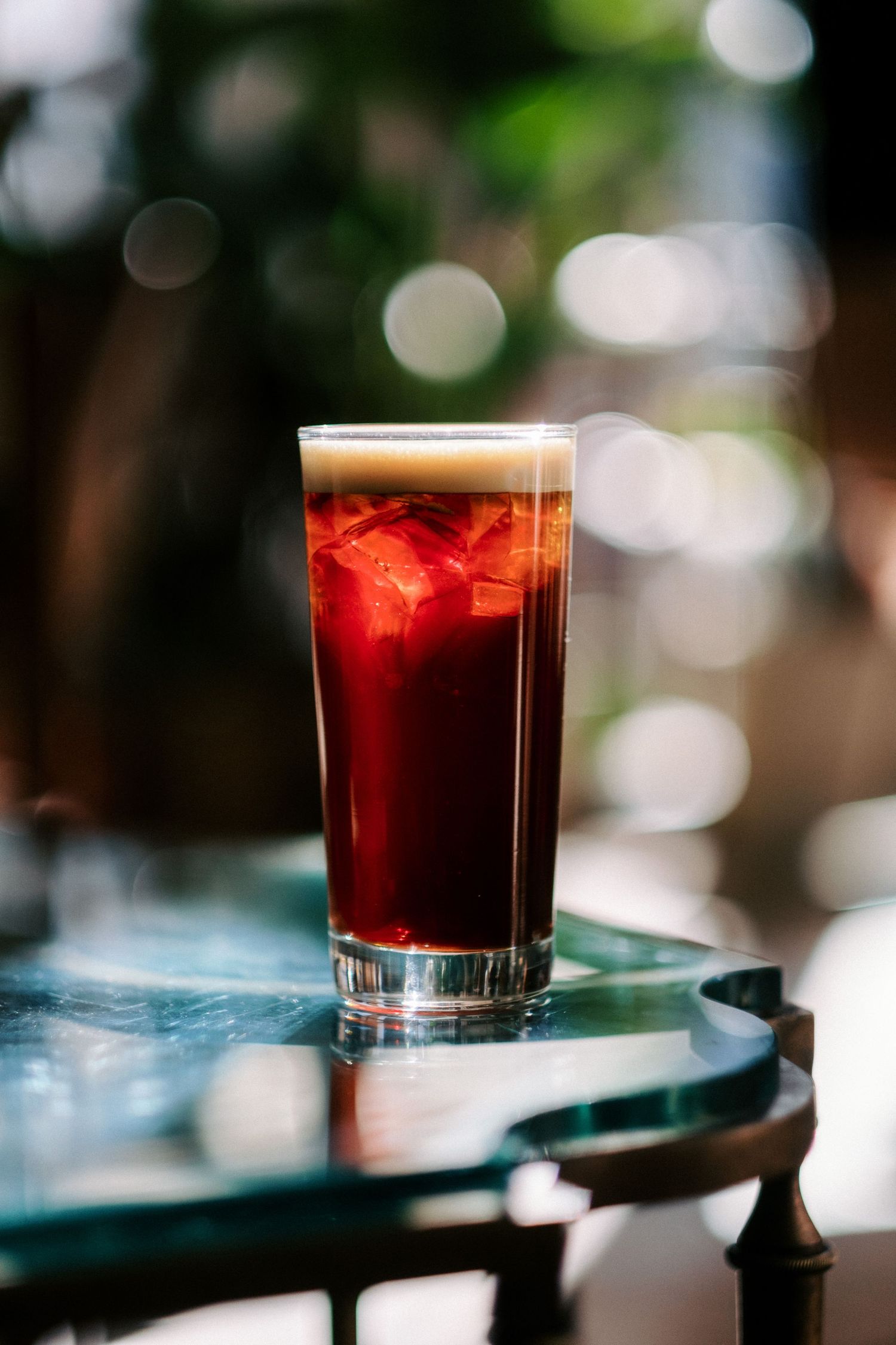 Dark red cocktail served in a glass with bokeh background effect.