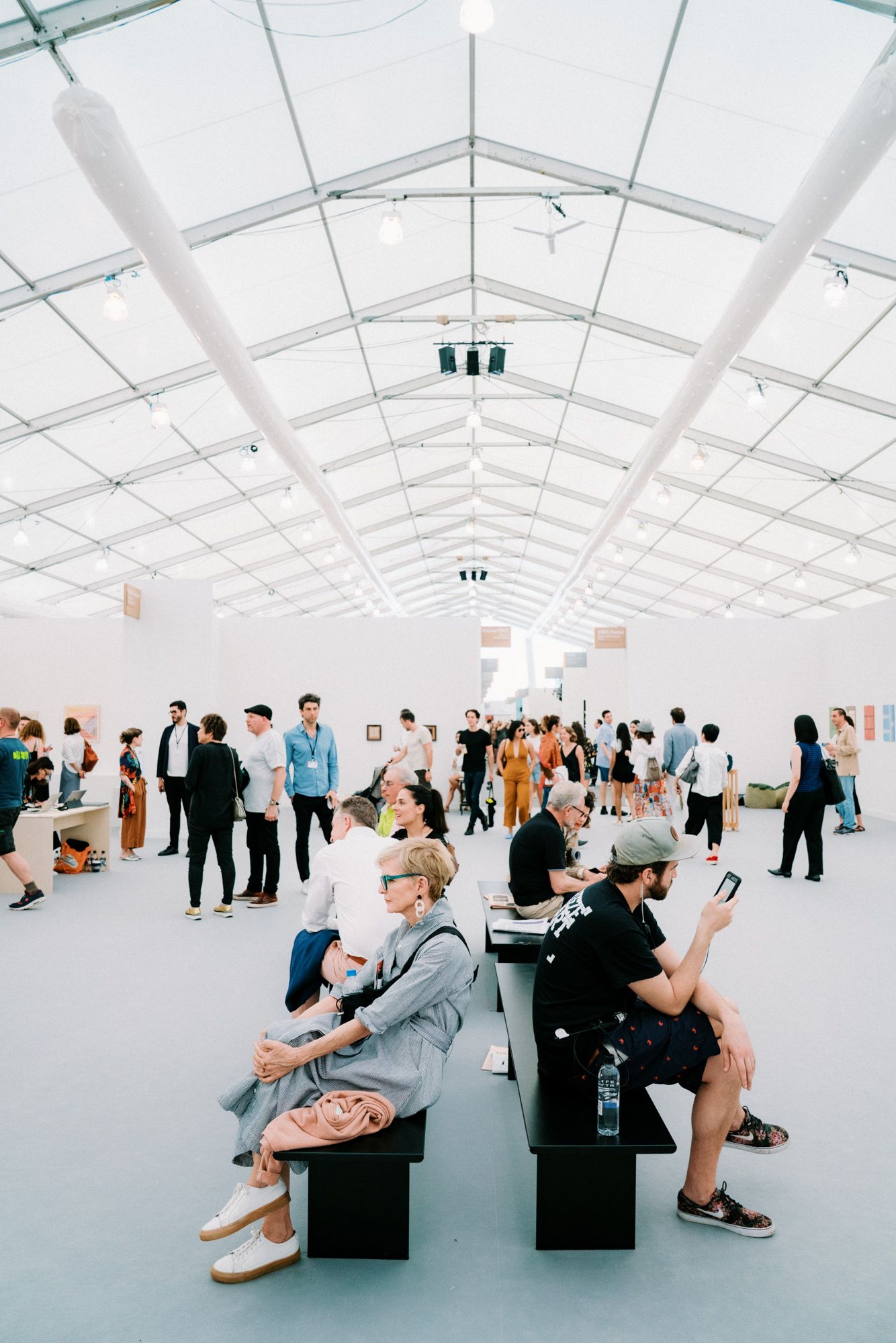 Visitors browse and socialize inside a bright, modern art fair tent with white walls and natural lighting.