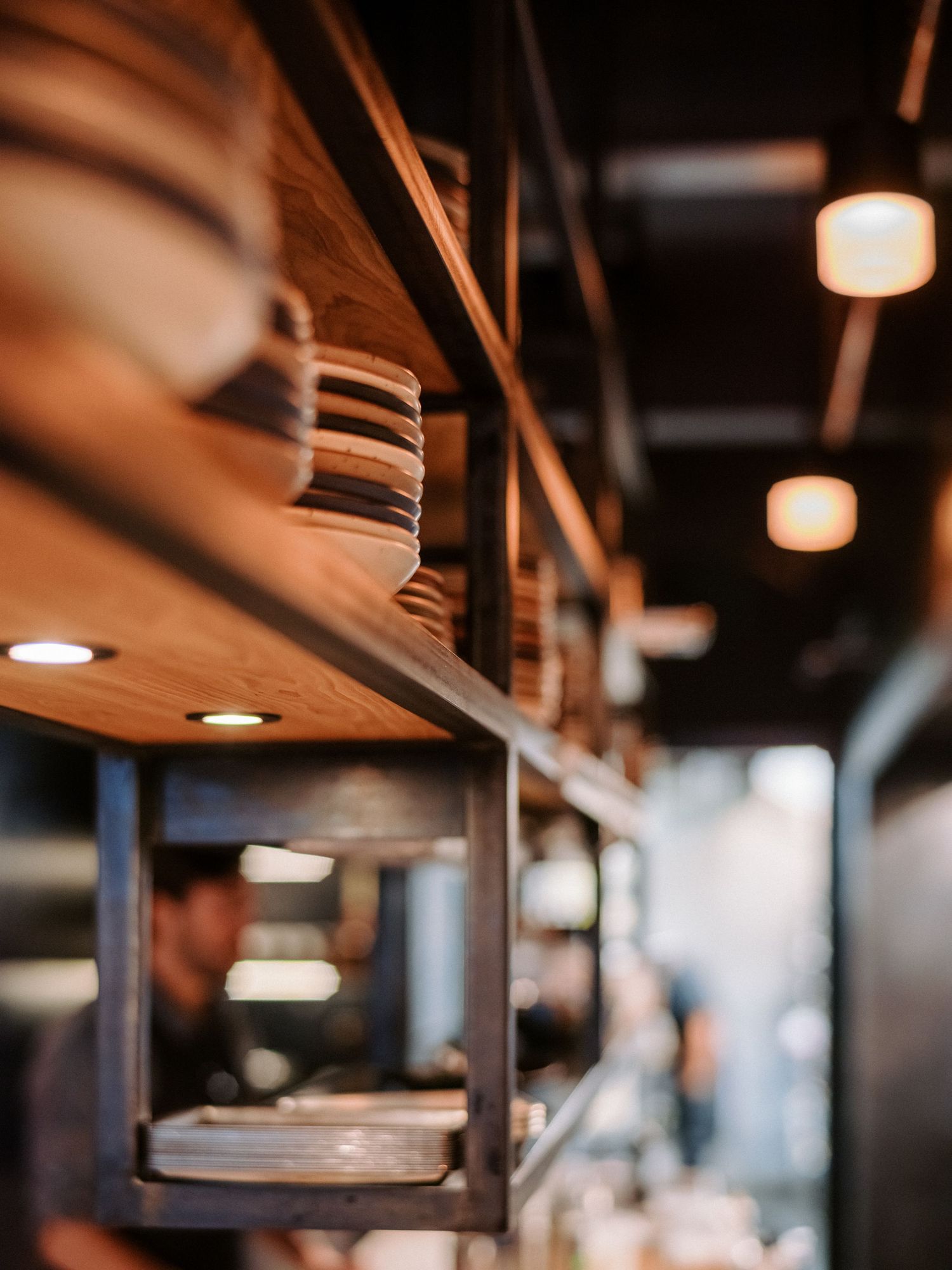 Warm lighting illuminates wooden shelving and industrial ceiling details in restaurant interior.