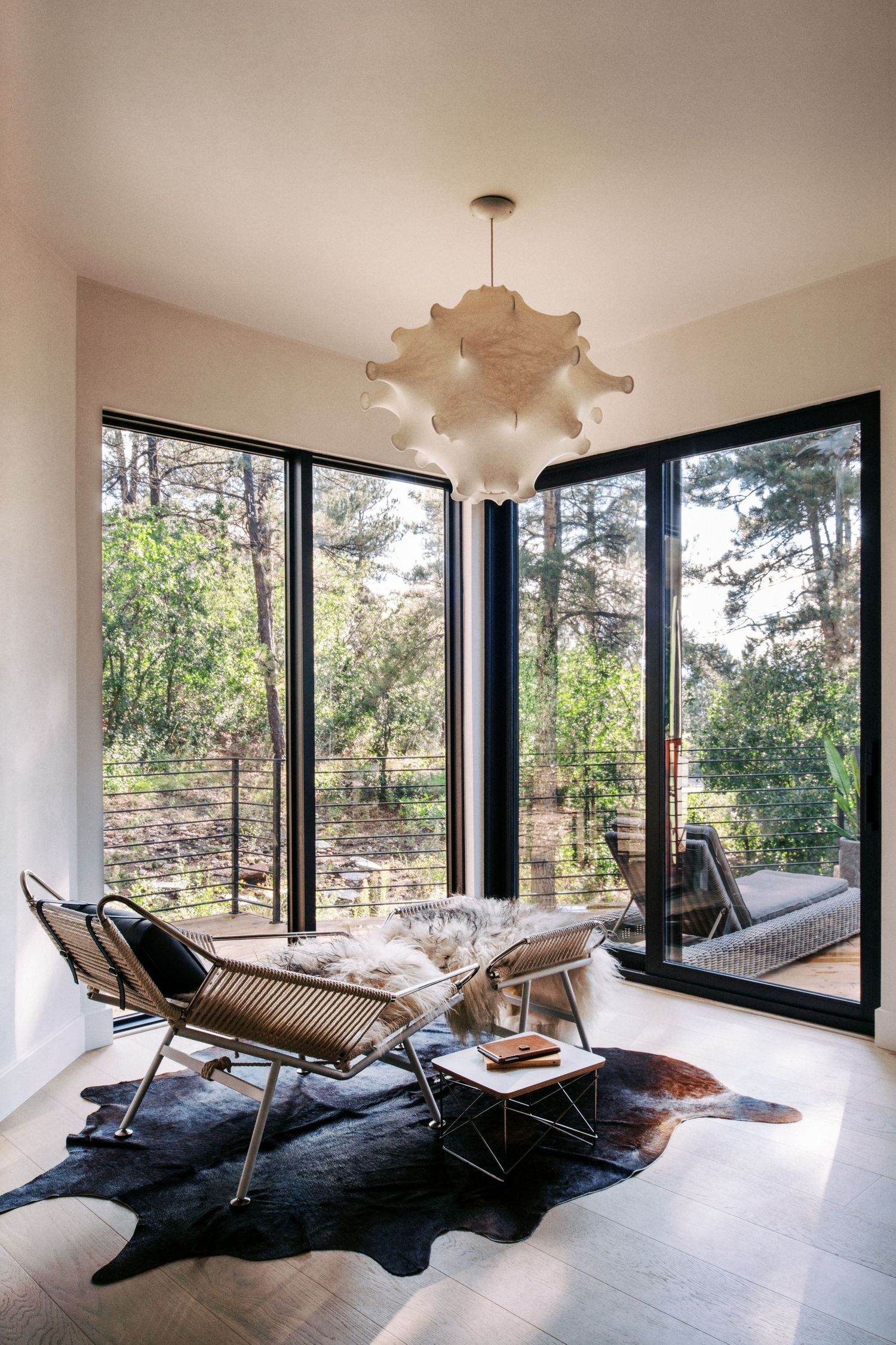 Contemporary living space with floor-to-ceiling windows and modern lounge chairs on cowhide rug.