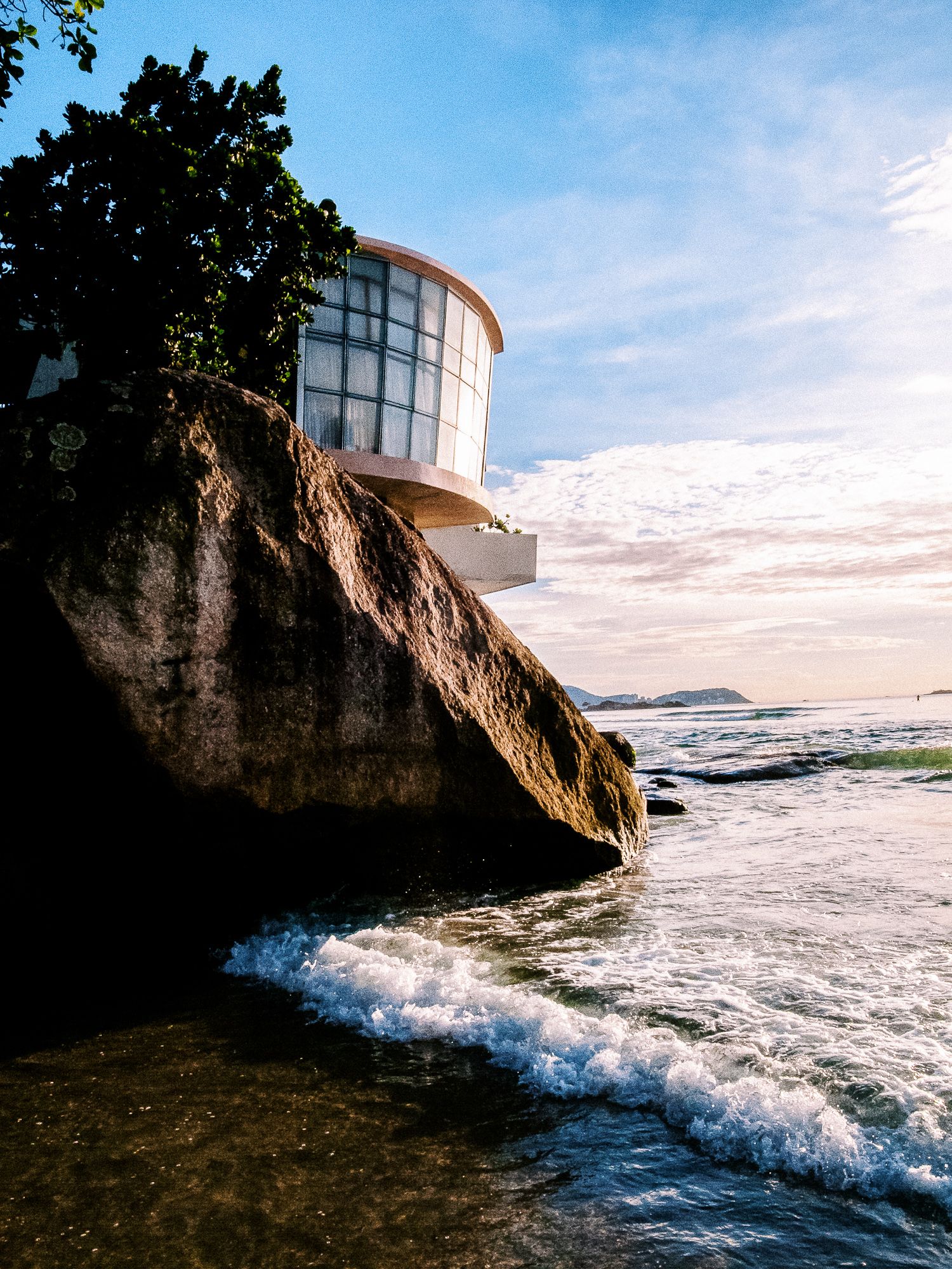 Lighthouse perched on rocky cliffs with crashing ocean waves below.