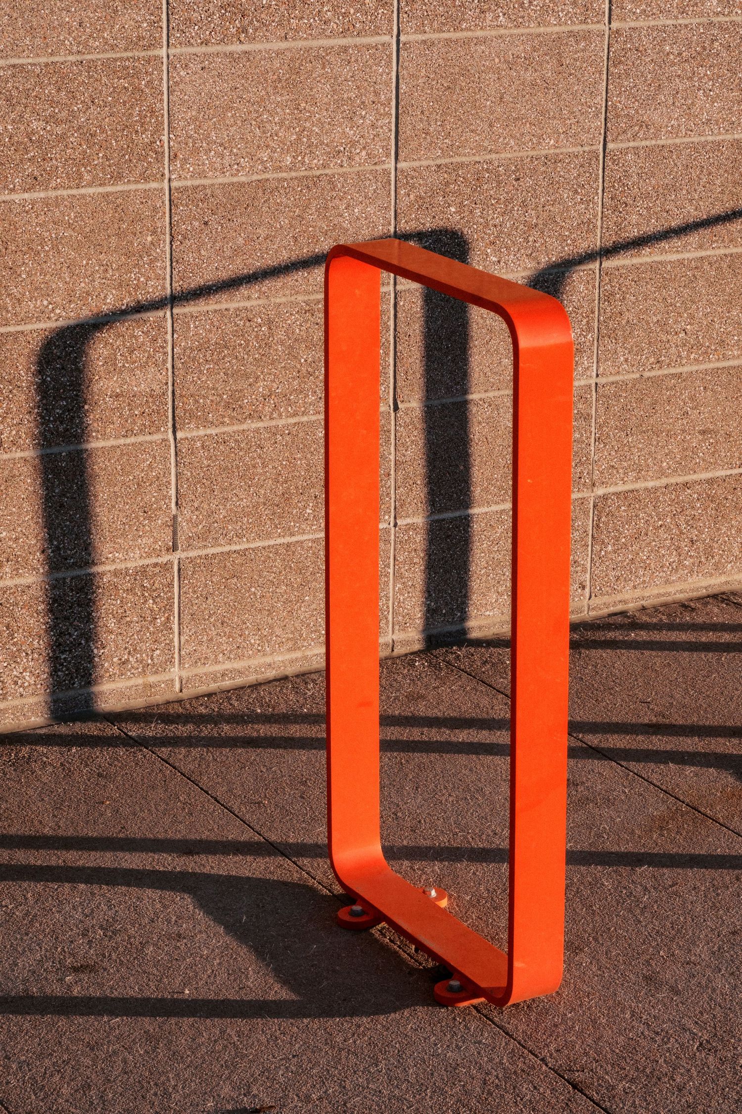 Orange metal bracket casting dramatic shadows on a textured concrete wall in sunlight.