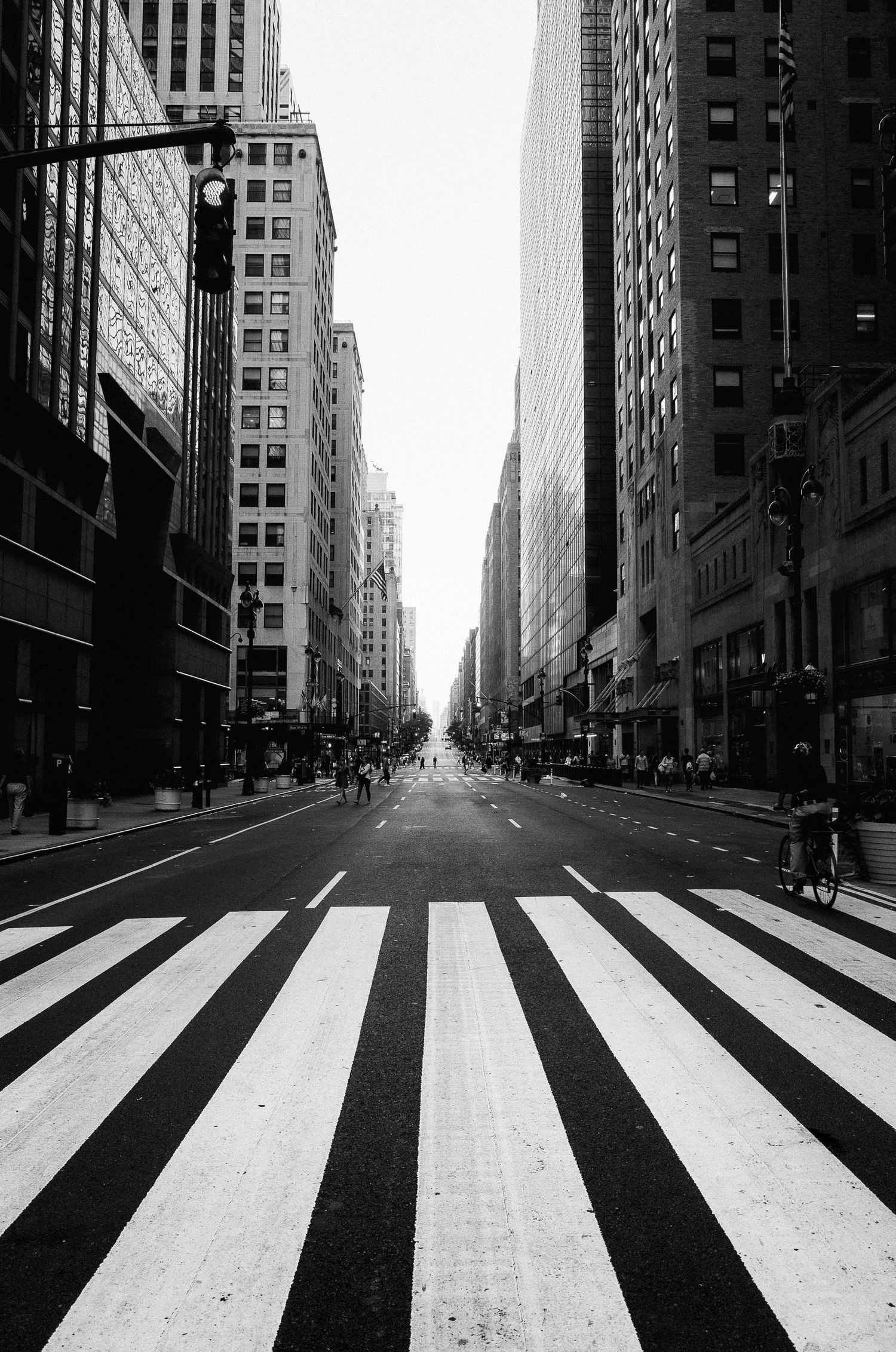 A black and white urban street view with dramatic zebra crossing stripes leading to tall skyscrapers in the distance.