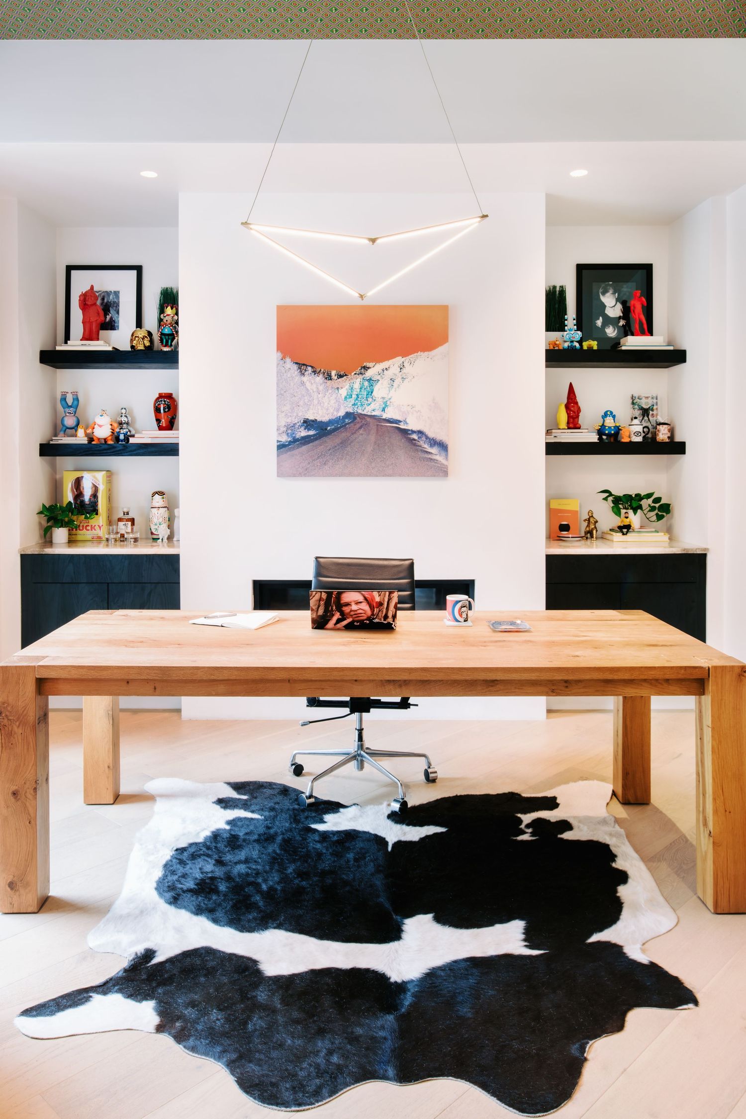 Modern dining room with wooden table and black cowhide rug features floating shelves displaying decorative items.