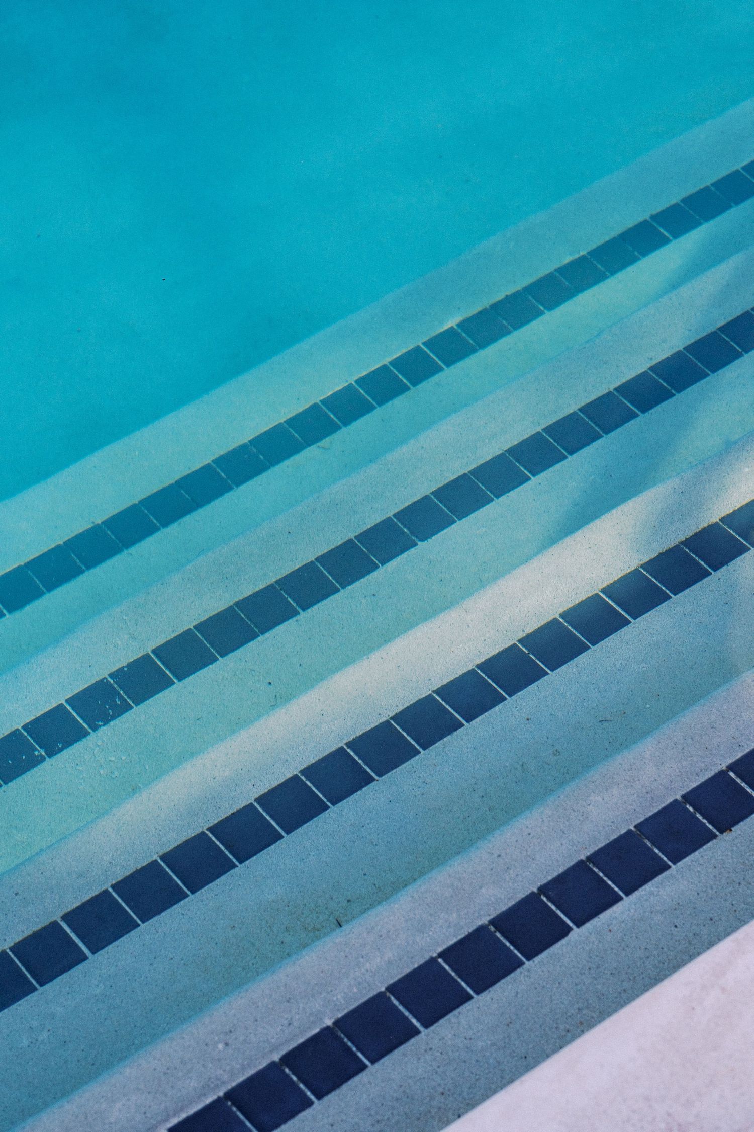 Abstract view of blue swimming pool steps with tiled stripe details.