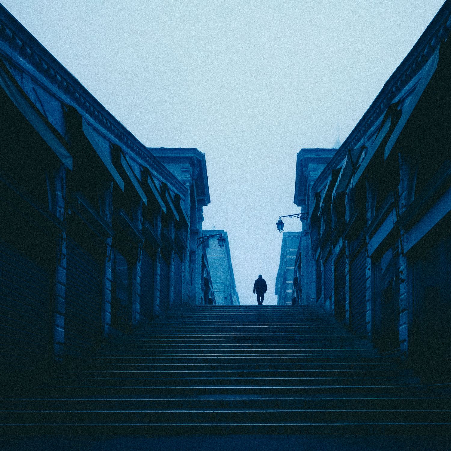 Dark blue-tinted stairway leads upward between stone walls with a silhouetted figure at the top.