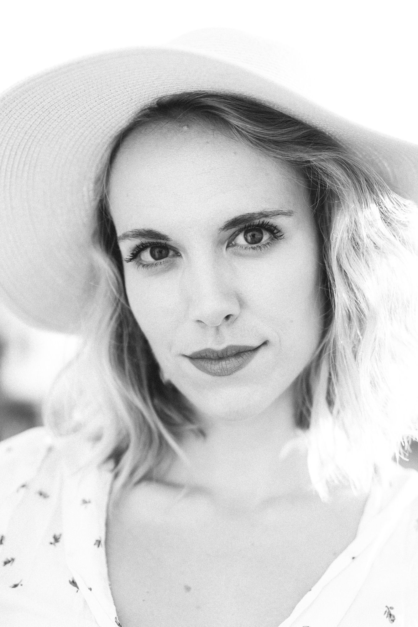 A black and white portrait of someone wearing a wide-brimmed sun hat and floral dress.