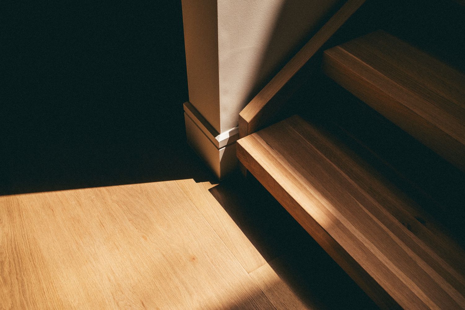 Close-up of wooden stairs and hardwood floor with warm sunlight casting shadows near a door frame.