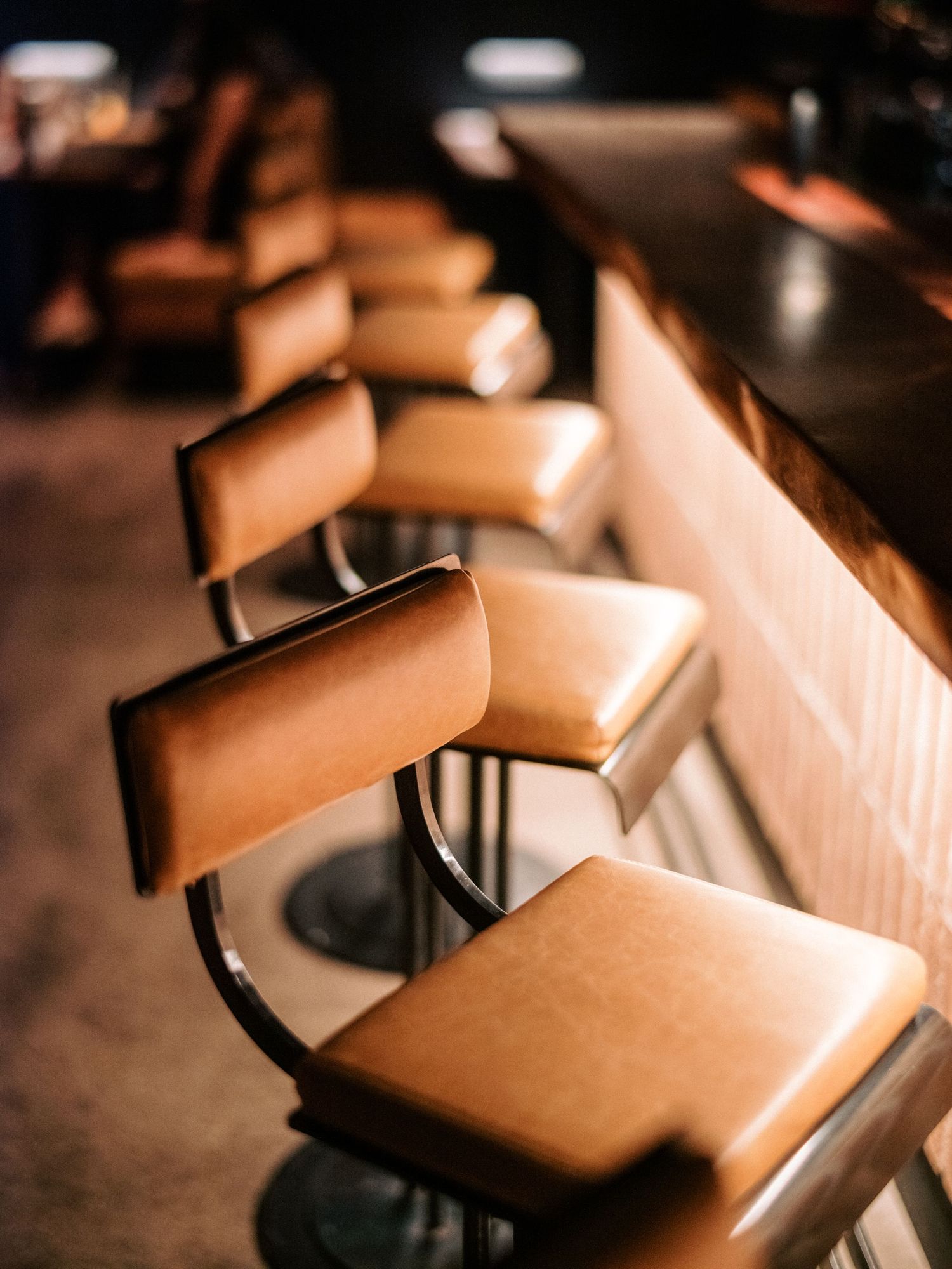 Row of leather bar stools along counter under warm restaurant lighting.