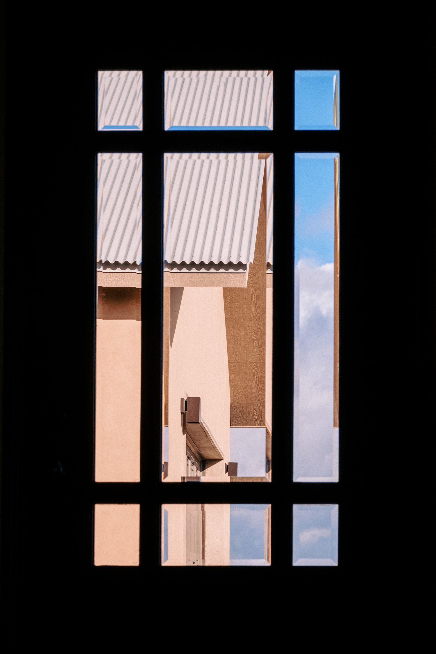 Geometric window frame silhouette with blue sky and beige building exterior visible.