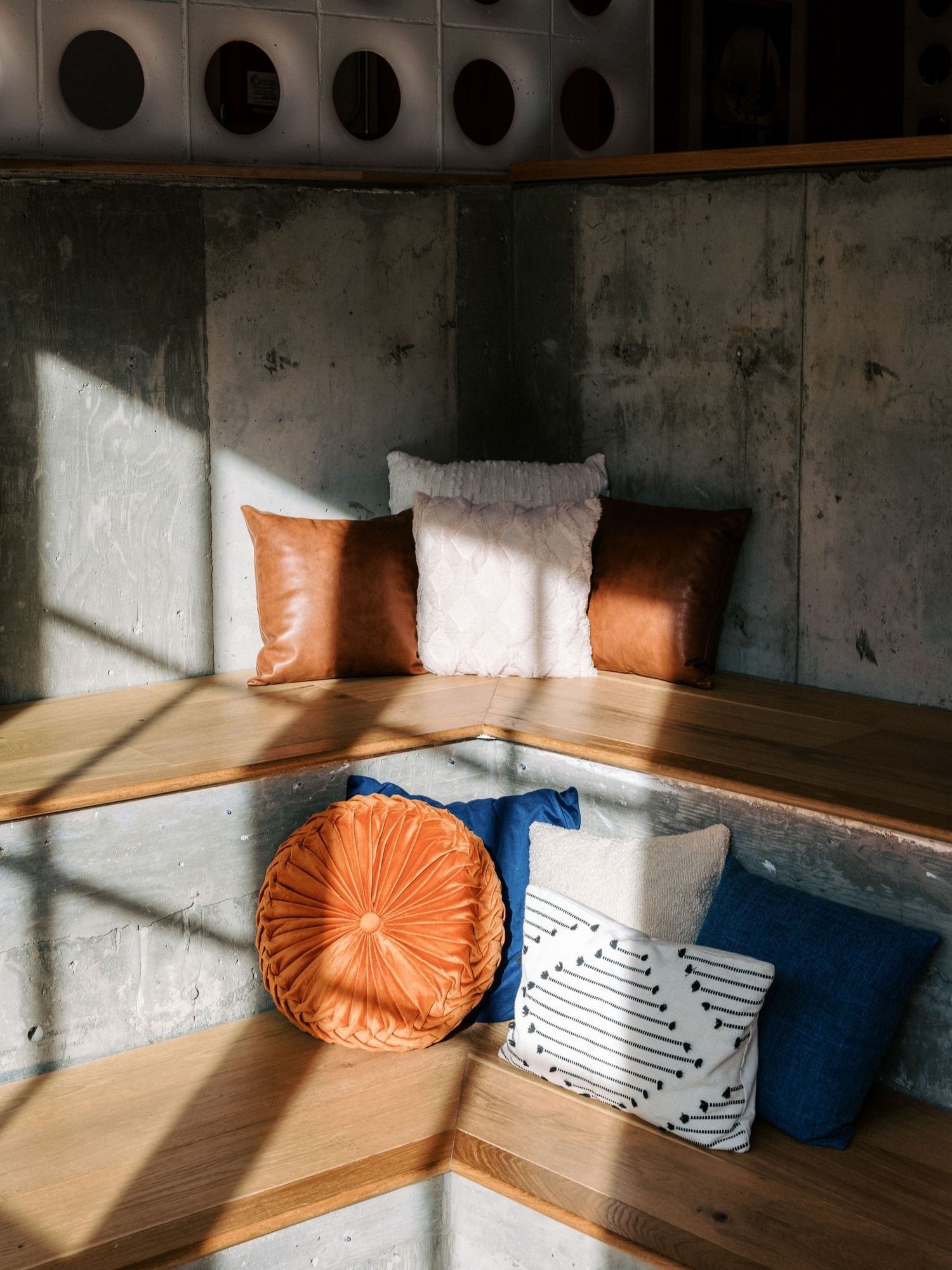 Modern seating area with orange and blue cushions arranged in a corner under natural lighting.