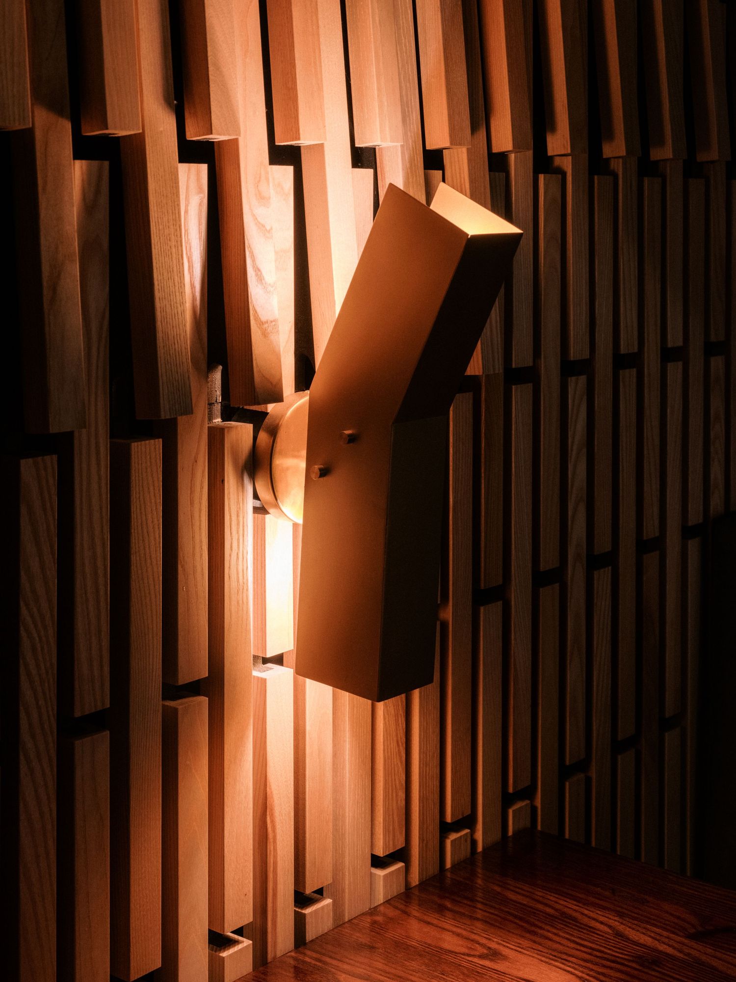 Modern wall sconce lighting fixture mounted on geometric wooden slat wall paneling.