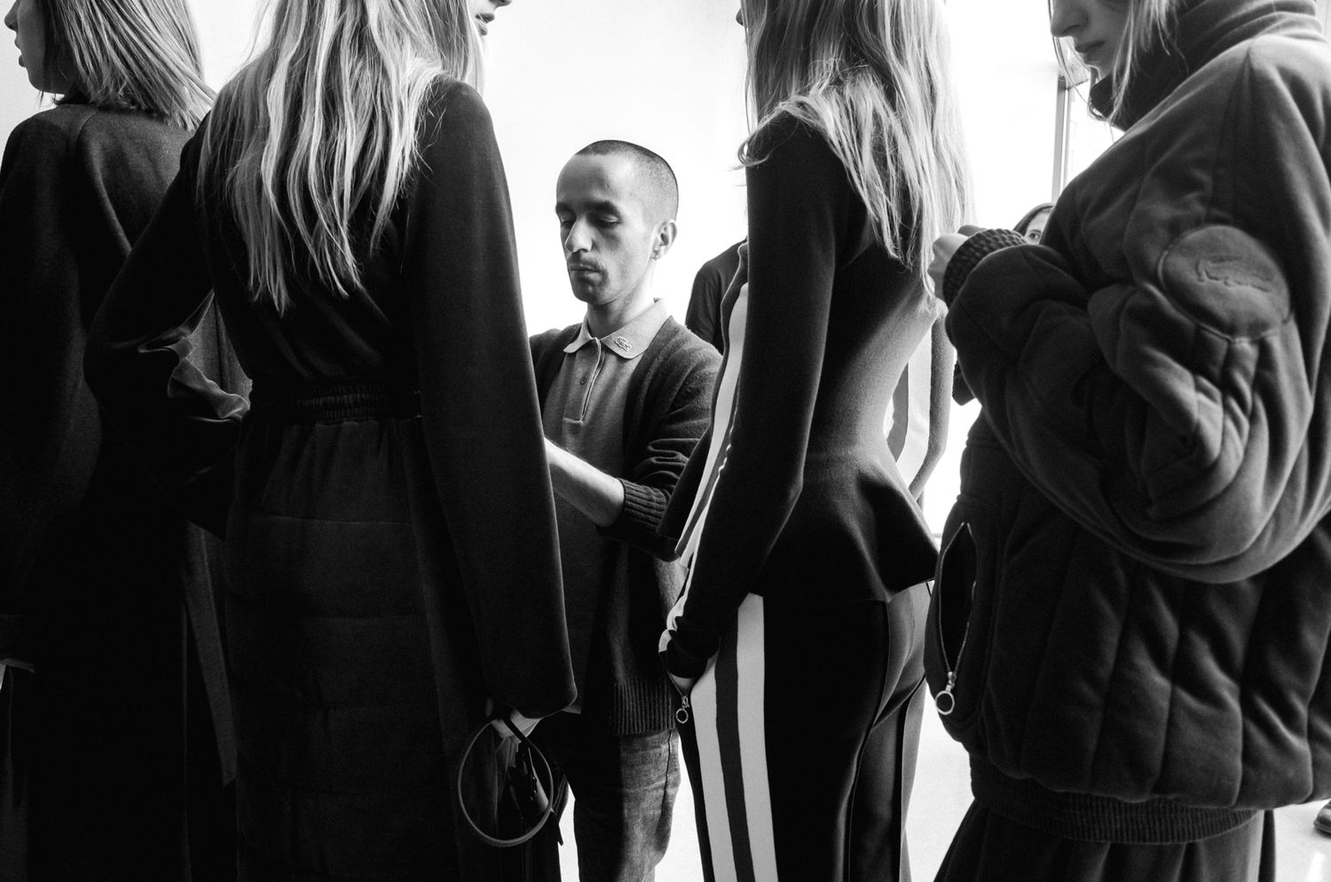 Black and white photo of a fashion designer fitting models backstage before a runway show.