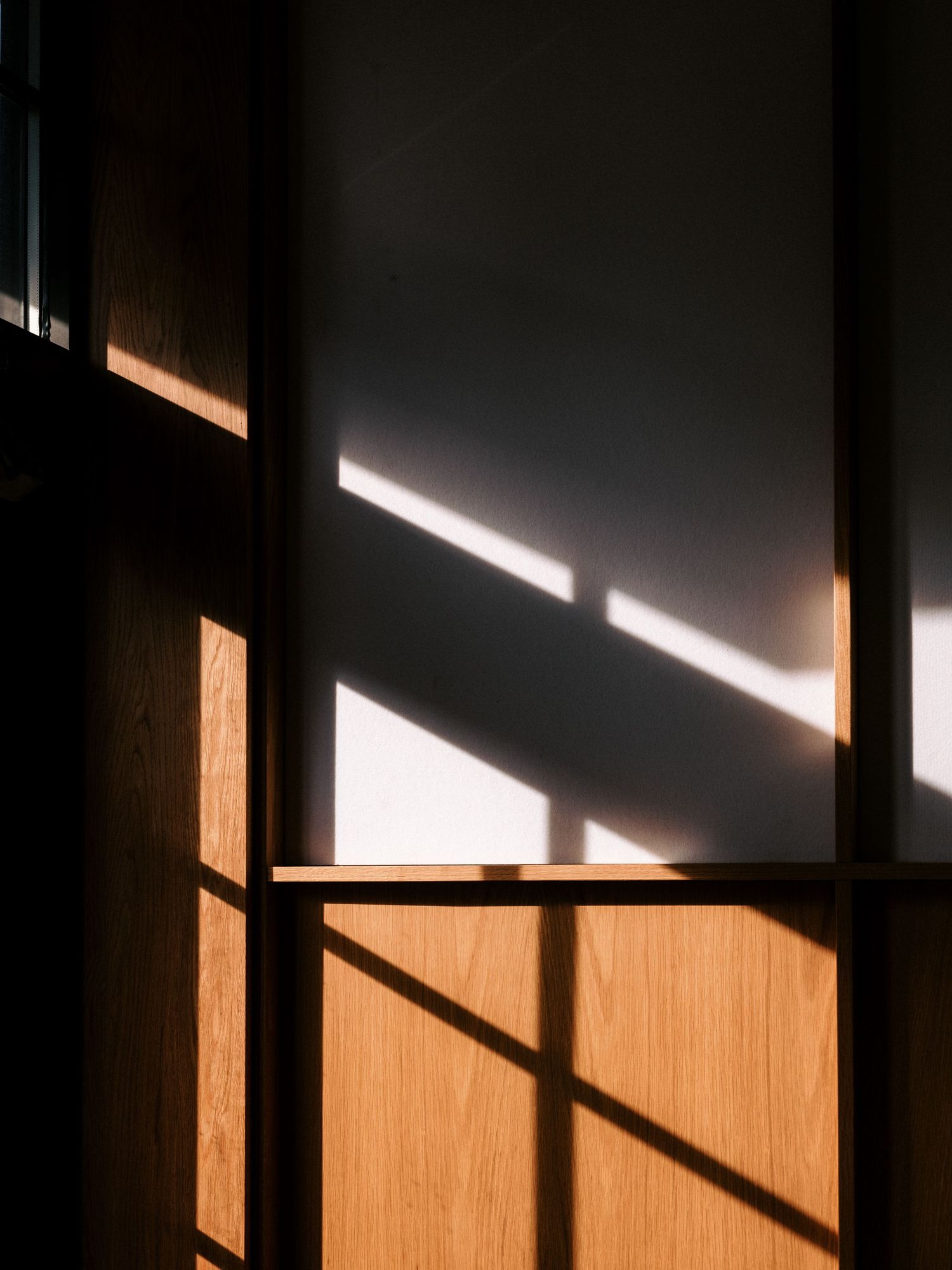 Dramatic angular shadows cast by sunlight on a wooden wall panel.