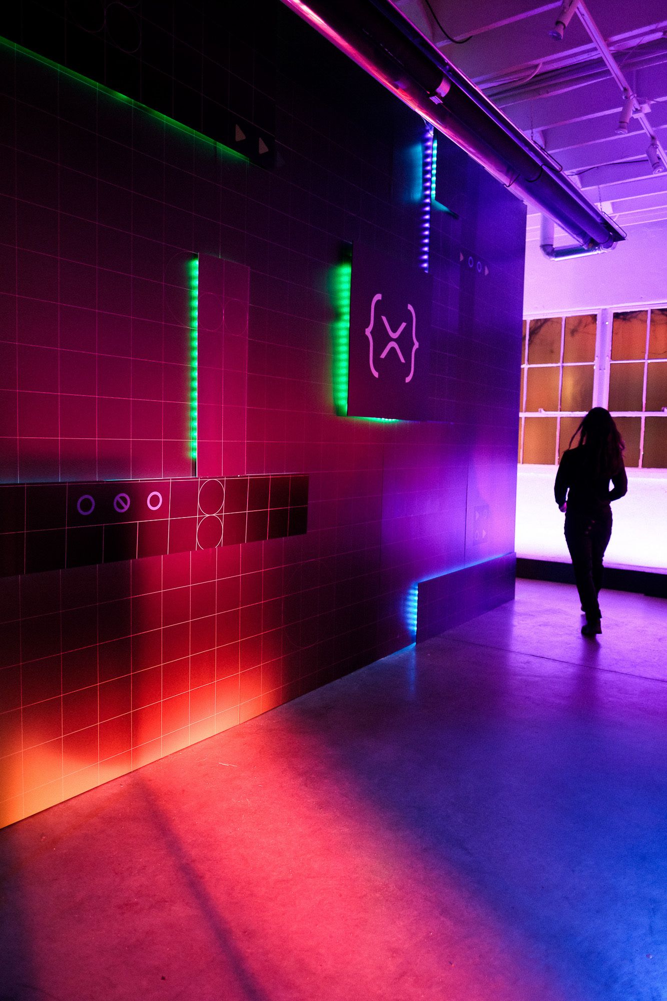 Neon-lit installation with colorful LED strips in red, green, and purple illuminating tiled walls with a silhouetted figure.