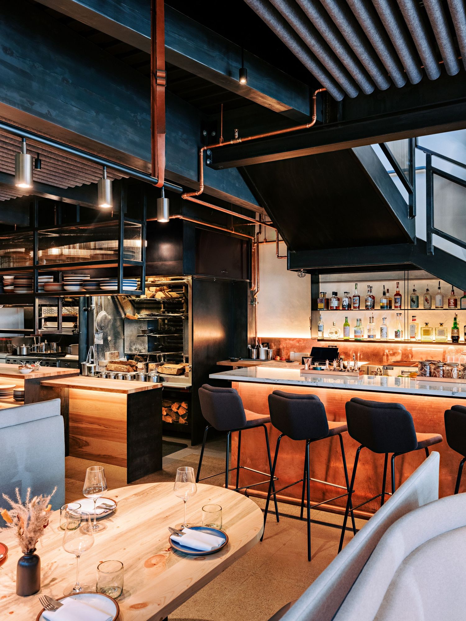 Modern restaurant interior with industrial design featuring a long bar and contemporary seating.