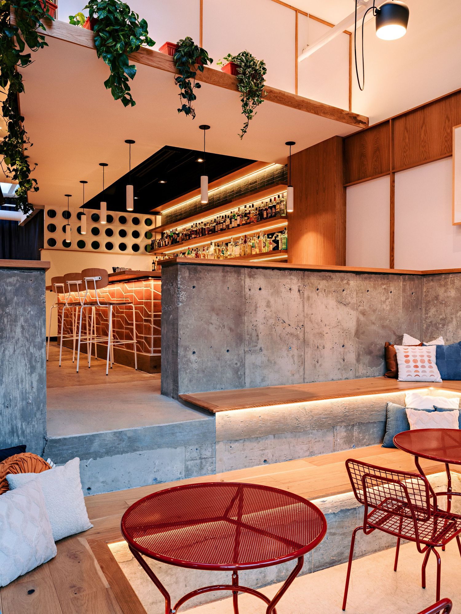 Modern restaurant space with red tables, concrete walls, and warm wood accents throughout.