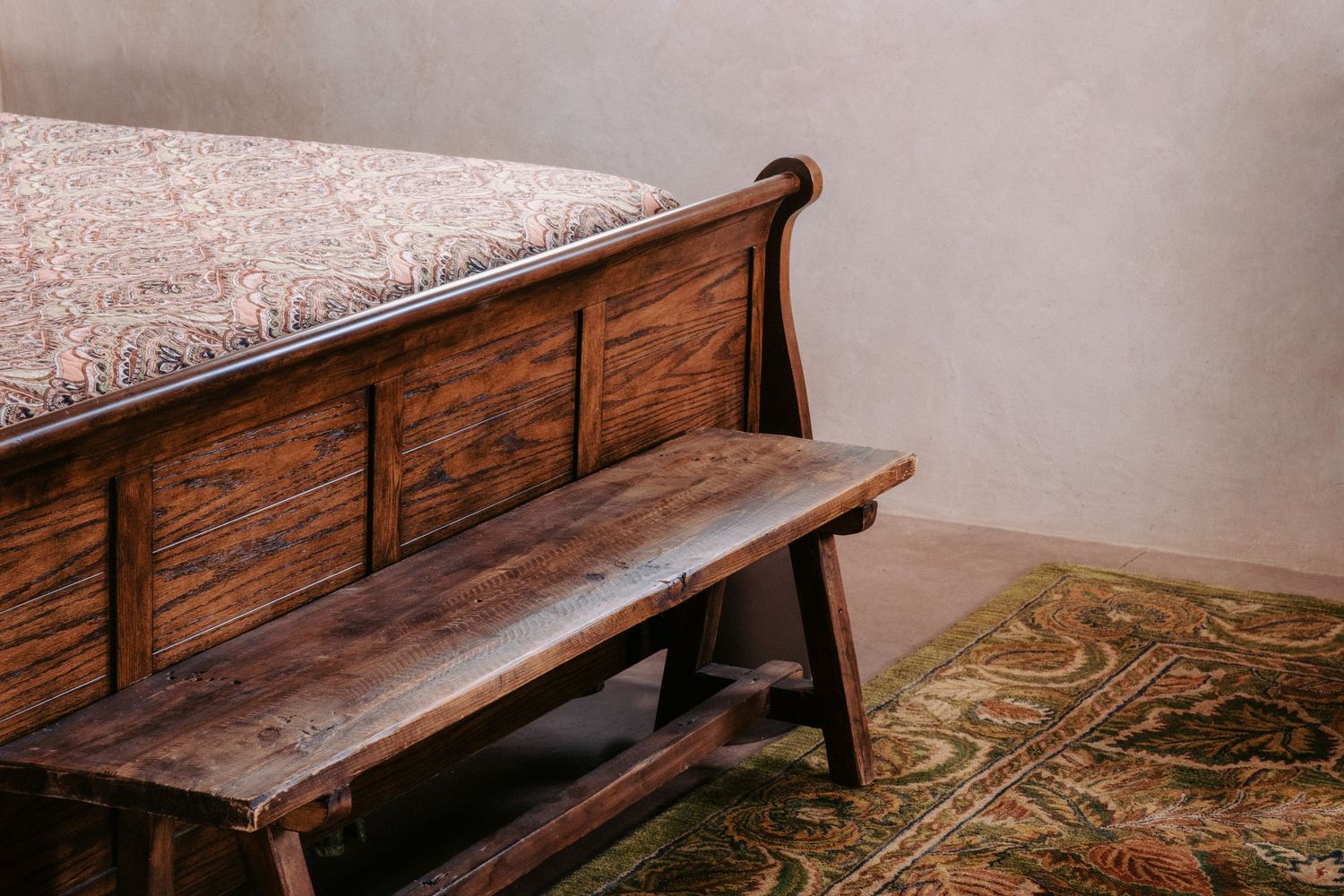 Rustic wooden church pew with ornate paneling sits against a textured wall with patterned carpet below.