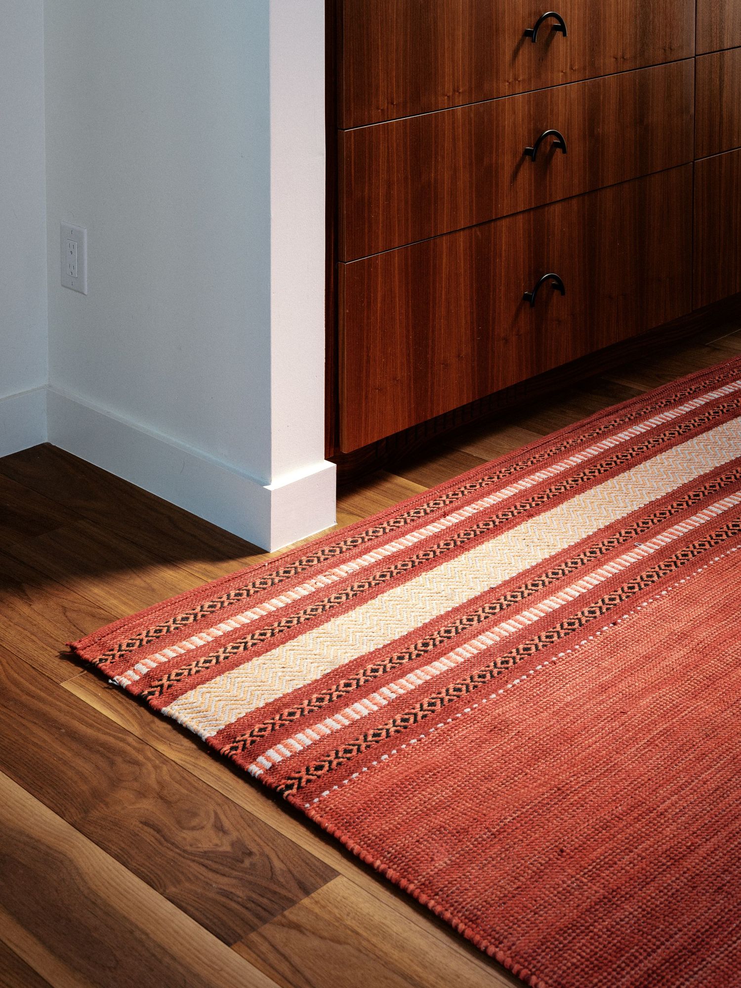 Wooden paneled wall with decorative palm tree details meets hardwood floor and geometric red runner rug.