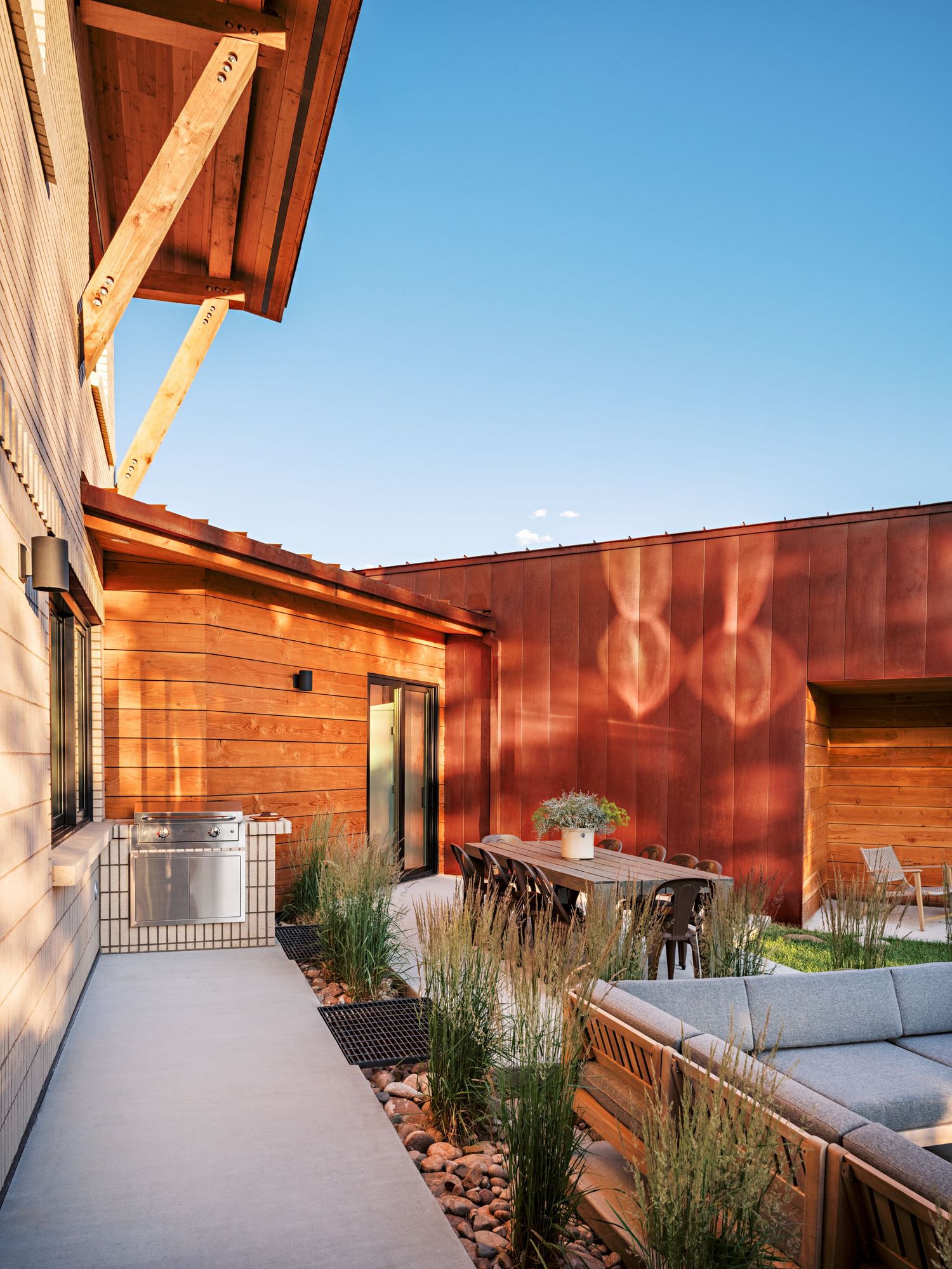 Outdoor patio space with modern furniture and wooden pergola against rustic red walls.