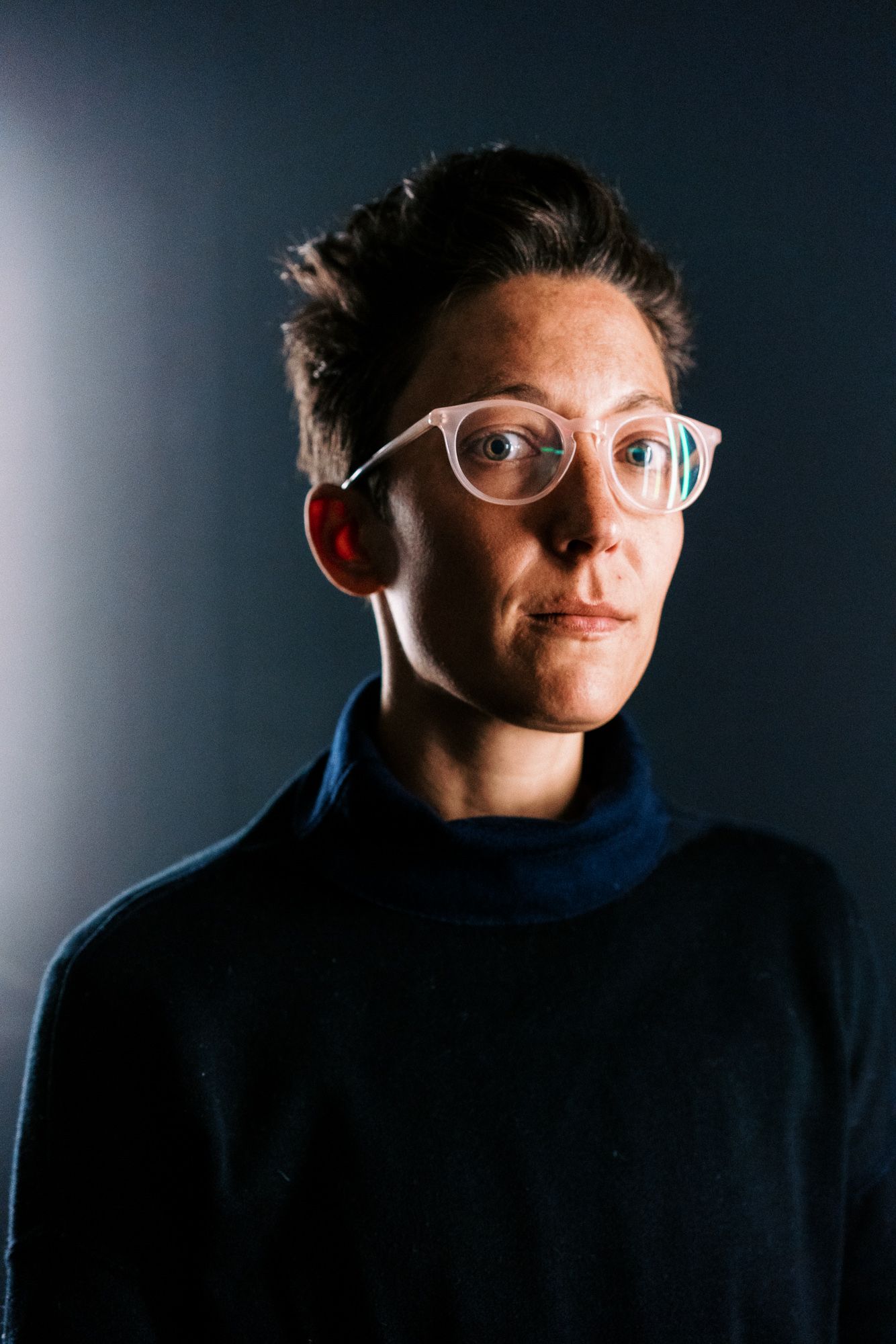 Portrait of person in glasses and navy sweater with dramatic side lighting.