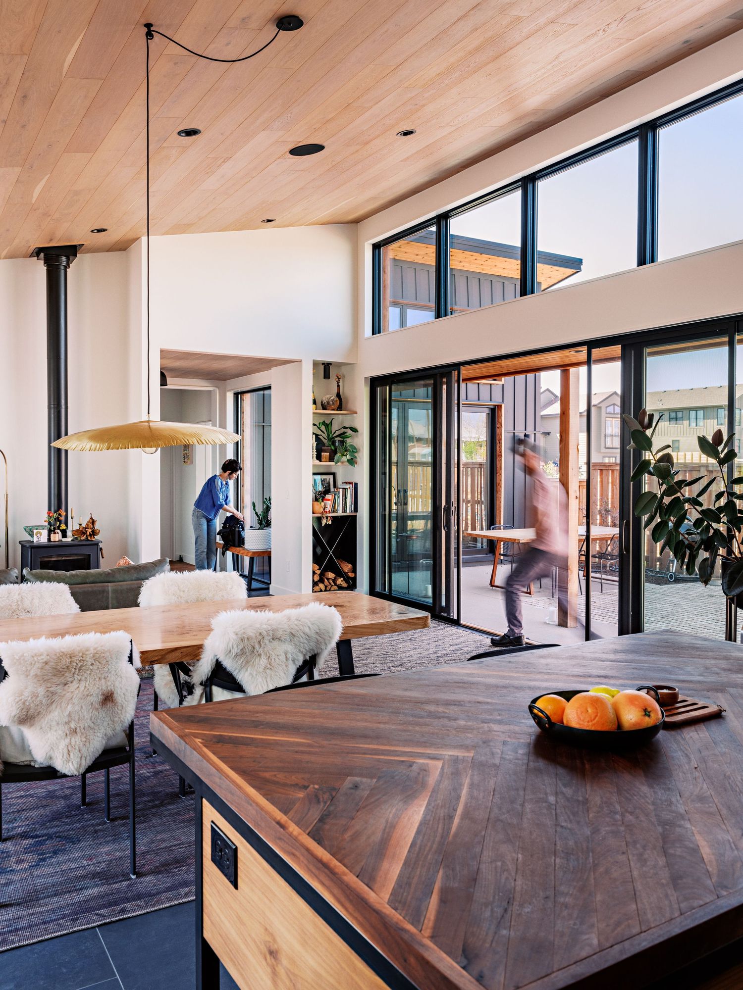 Spacious dining area with wooden herringbone table and sheepskin throws near floor-to-ceiling windows.