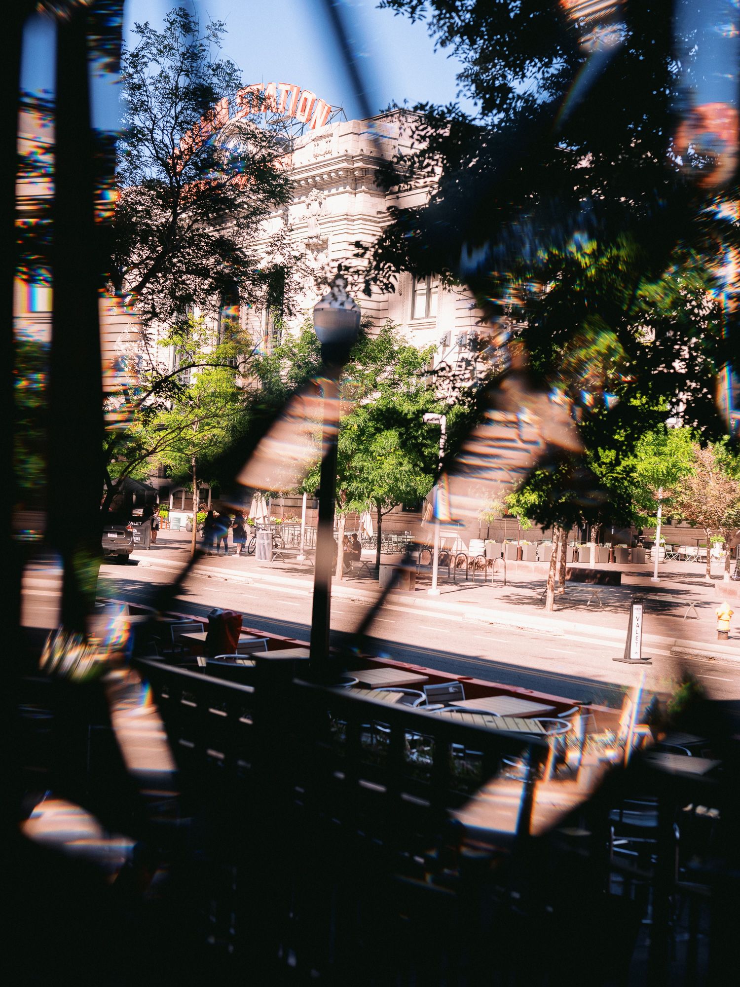 Blurred urban scene with trees casting shadows across a street view.