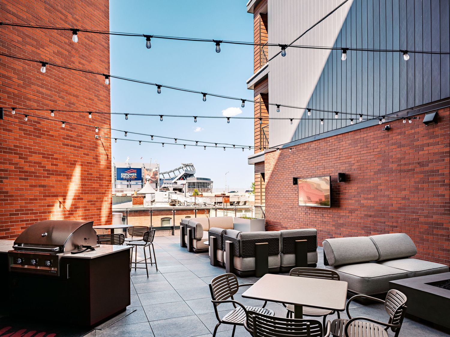 Modern rooftop terrace with string lights and comfortable seating areas against brick walls.