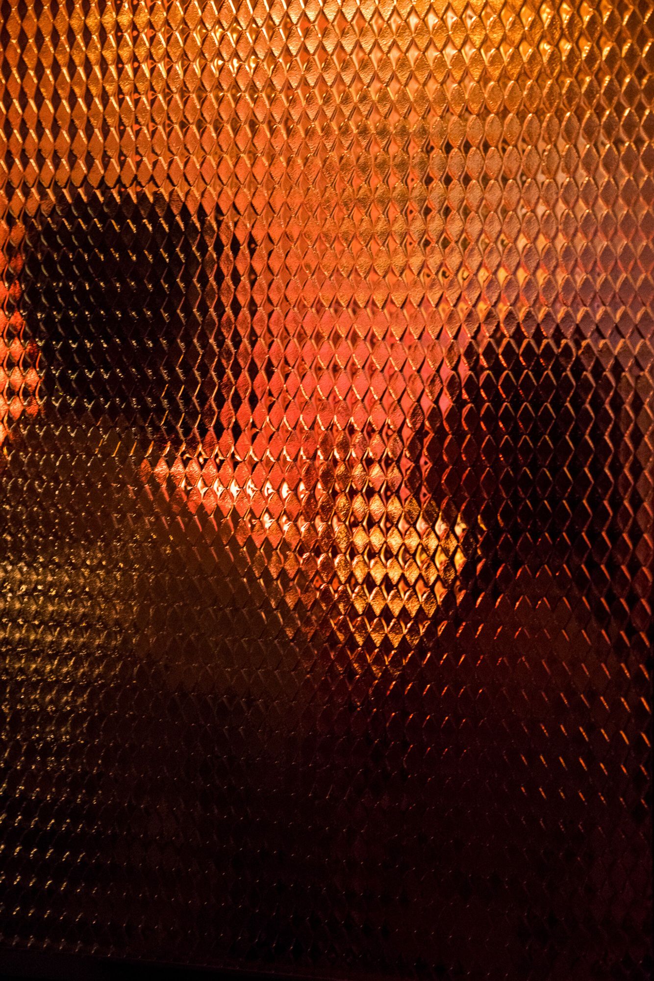 Abstract orange and red diamond patterned glass with silhouettes visible through the textured surface.