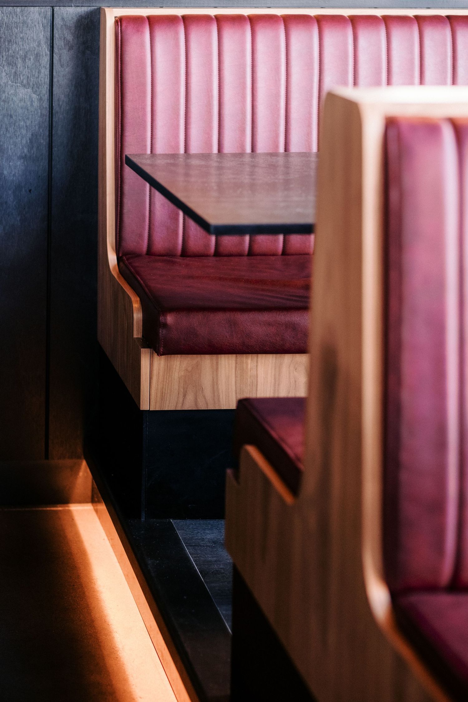 Pink leather booth seating in a modern restaurant interior with dramatic lighting.