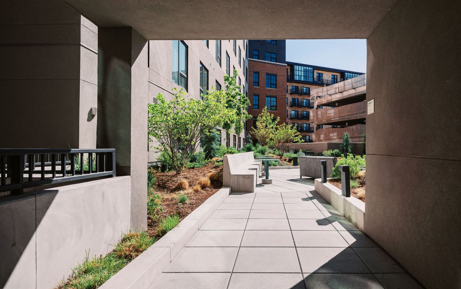 Concrete walkway between modern buildings with landscaping elements.