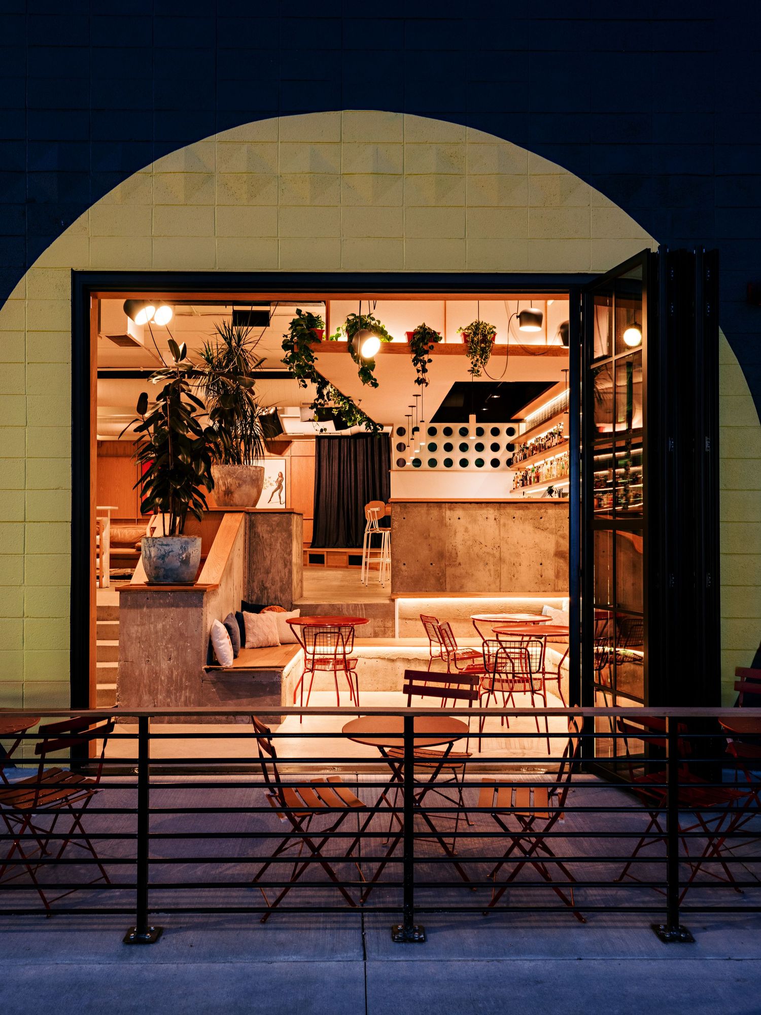 Warm interior view through arched windows showing restaurant seating and decor at night.