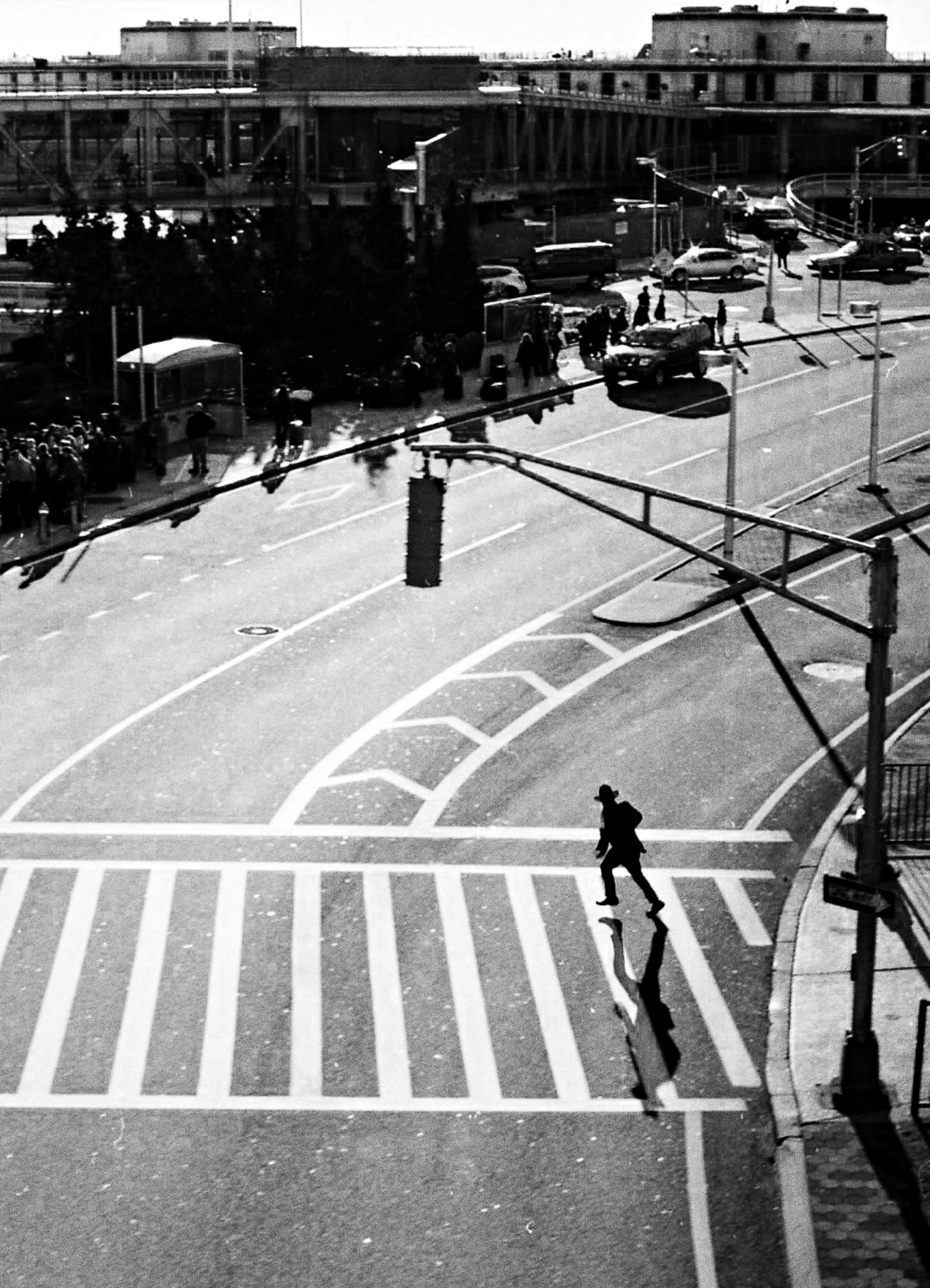 A black and white aerial view of an urban intersection with a lone pedestrian crossing the crosswalk.